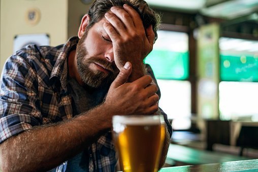 Sad man pictured looking at beer glass while sitting in beer bar | Photo: Getty Images