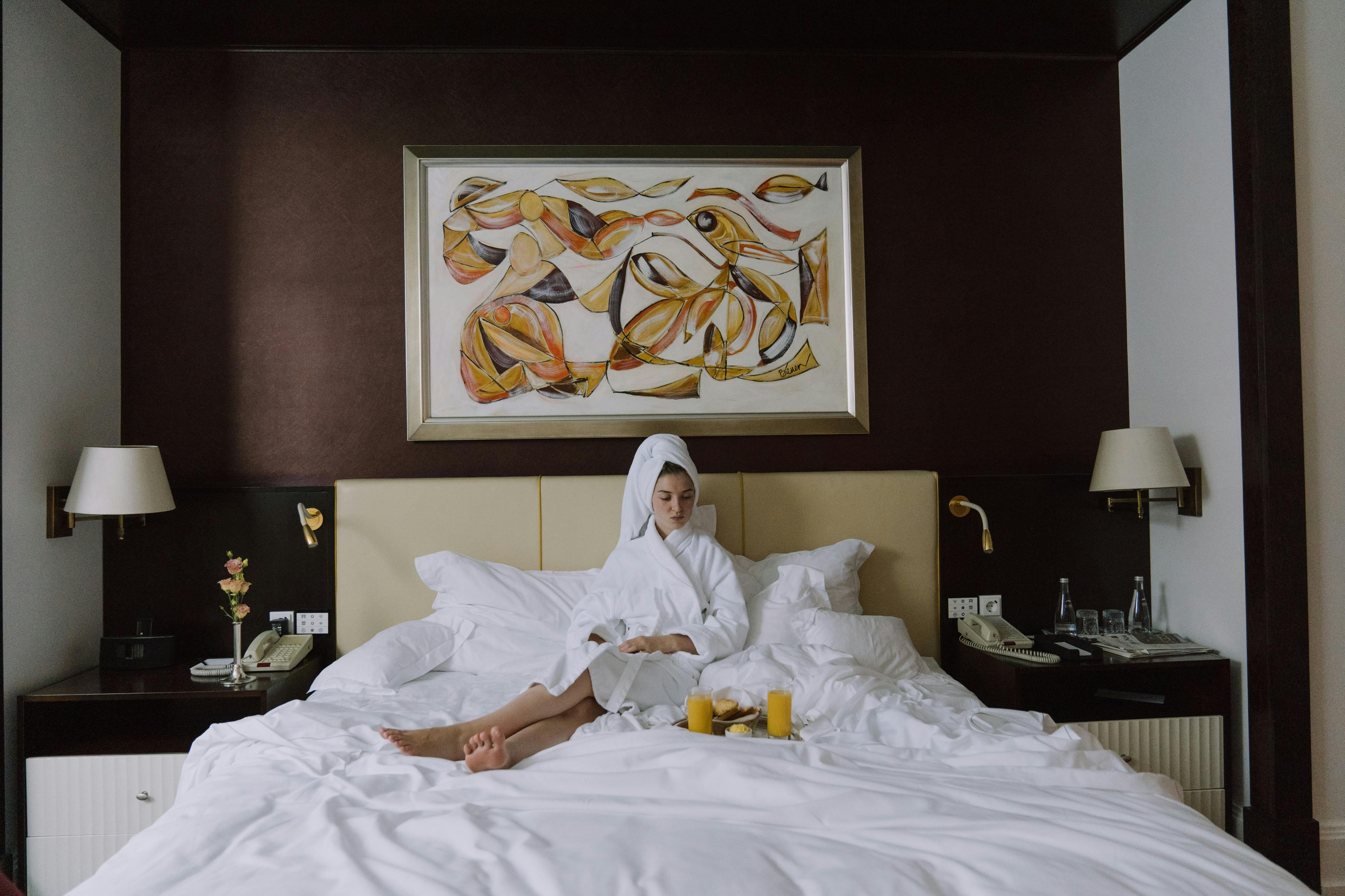 An upset woman sitting on a hotel room bed in a bathrobe | Source: Pexels