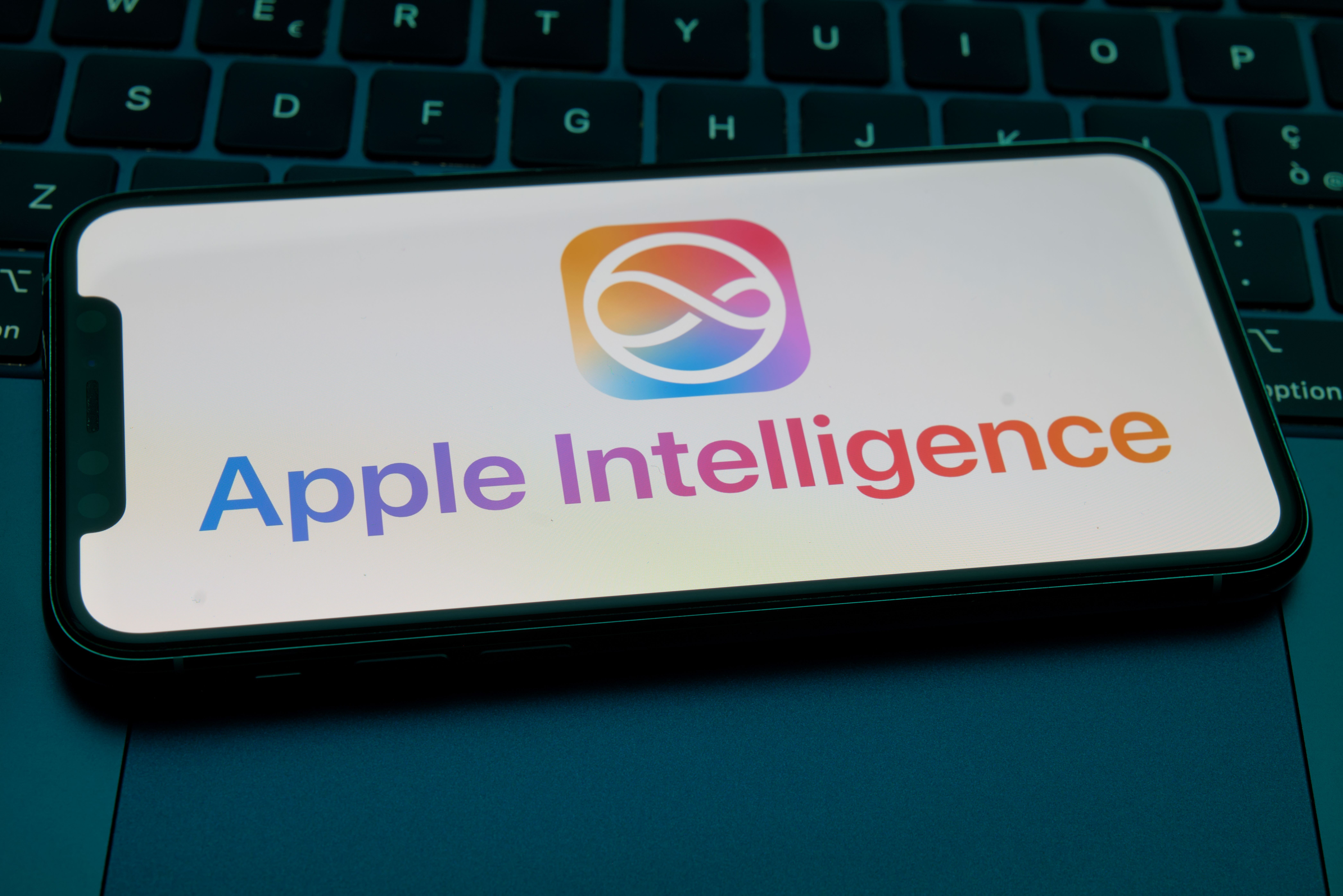 The Apple Intelligence logo and text display on an iPhone screen, resting on a dark laptop keyboard in San Ferdinando di Puglia, Italy, on December 23, 2025 | Source: Getty Images