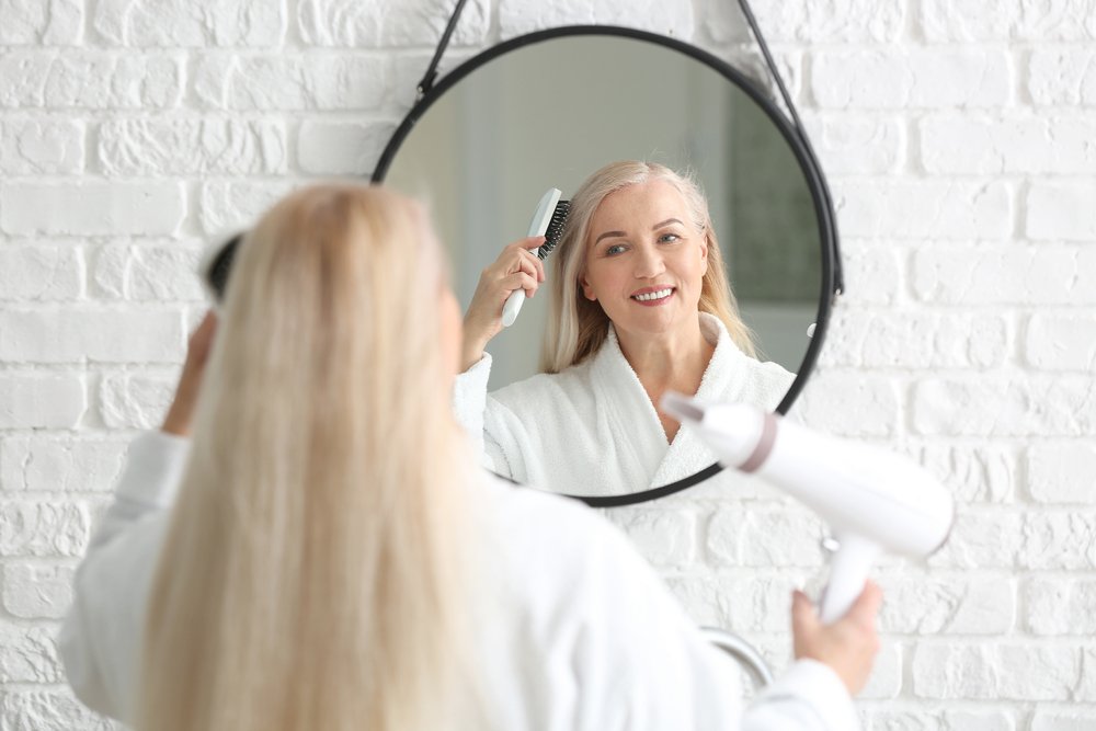 Modelo usando su secadora de pelo frente al espejo. | Foto: Shutterstock