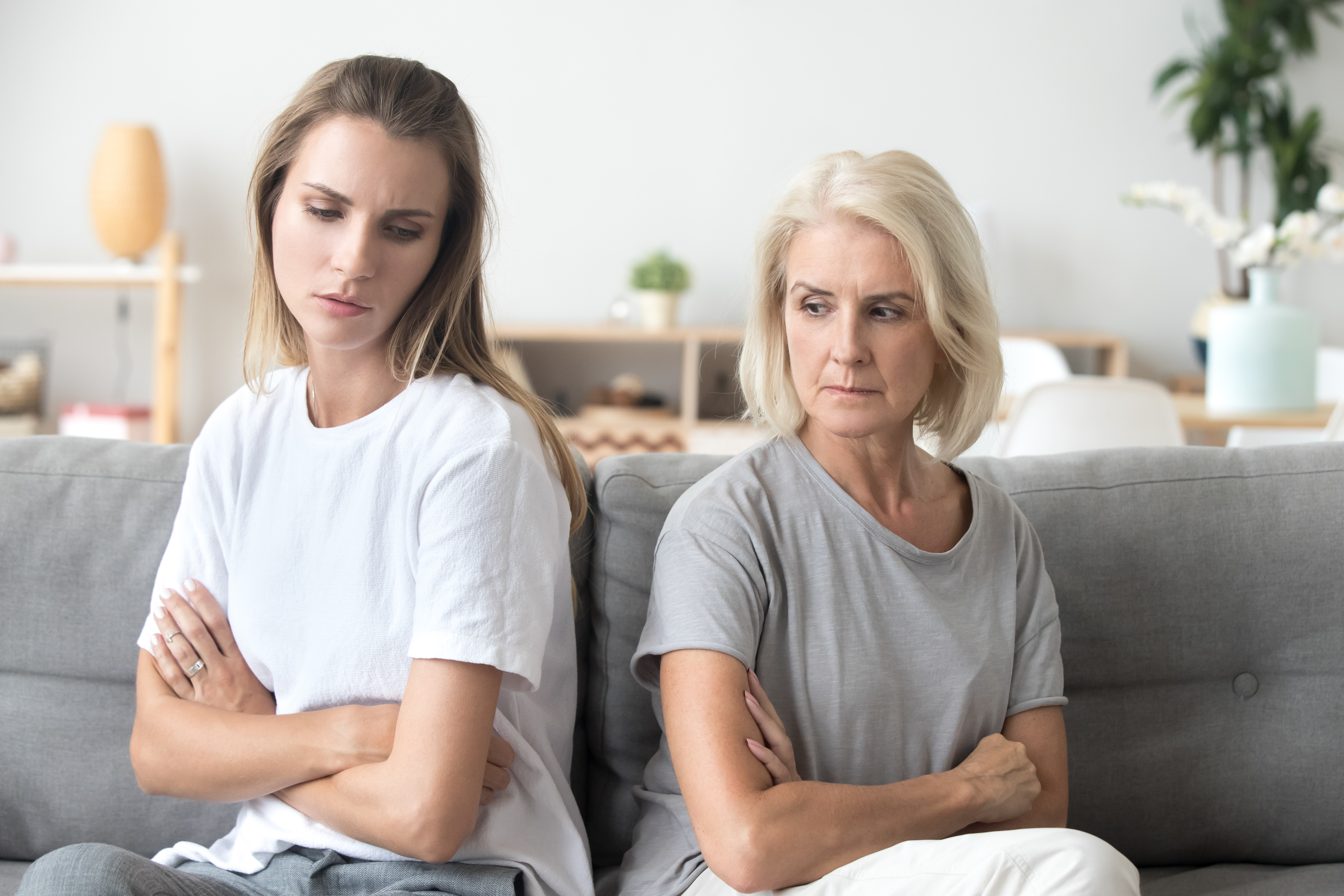 A younger woman suspicious of an older woman, both seated with their backs turned to each other | Source: Shutterstock