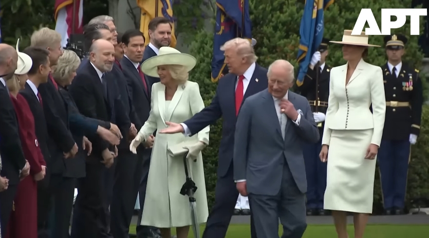 With Queen Camilla mid-handshake, Donald Trump gestures toward the next official as if directing the flow, while King Charles III glances aside, the trio briefly overlapping in what appears to be an unscripted moment. | Source: YouTube/APT