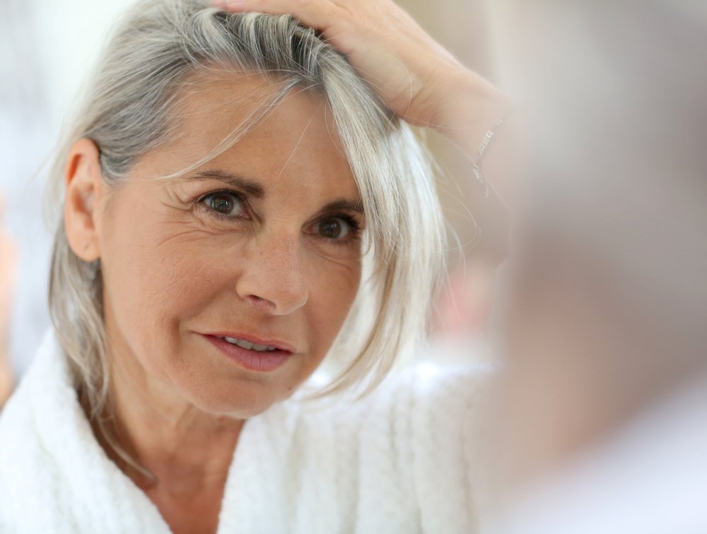 Mujer madura con cabello gris mirándose al espejo. | Foto: Shutterstock