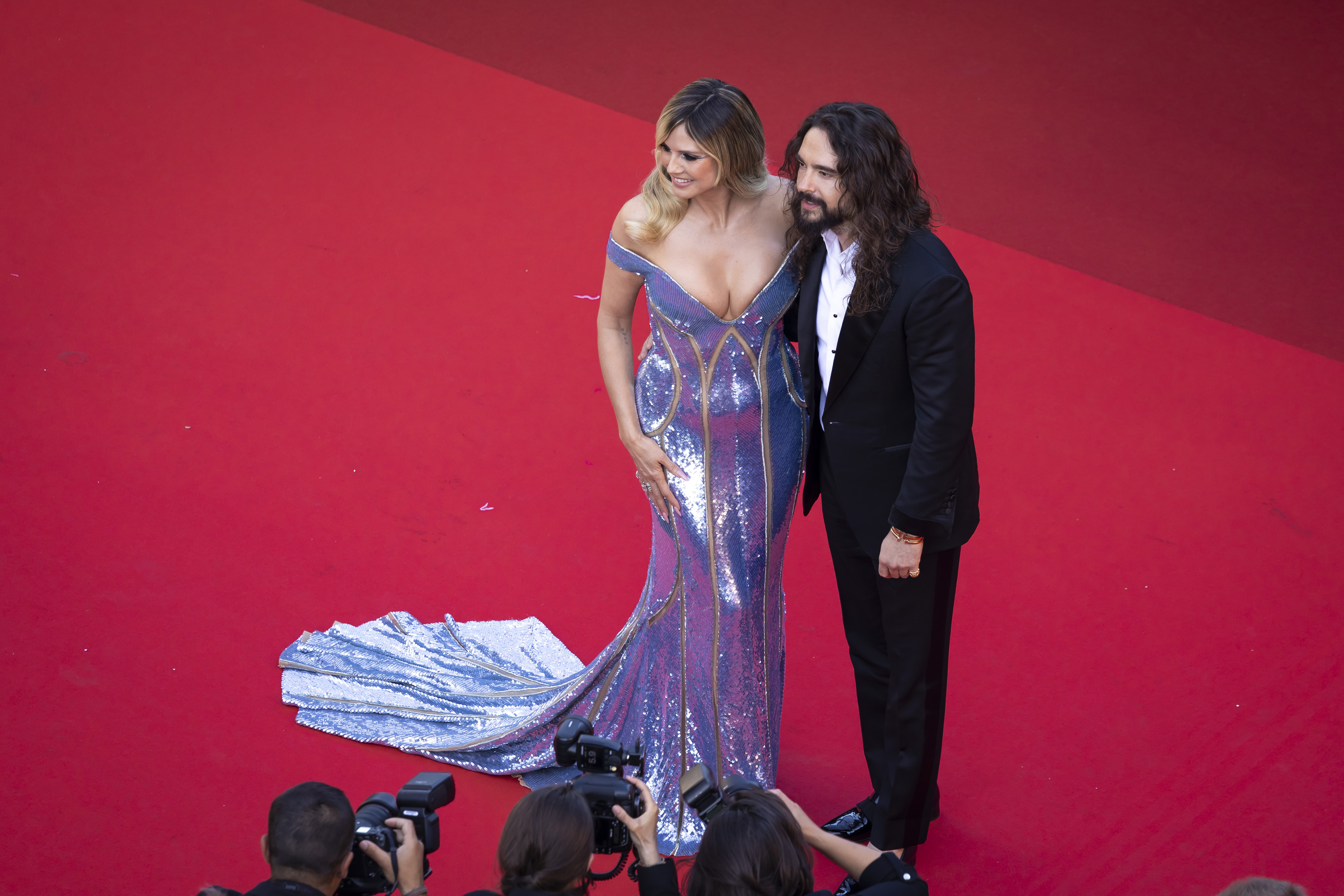 In an aerial shot, Kaulitz and Klum stand side by side, perfectly complementing each other in both attire and aura. Their coordinated elegance and shared presence create a striking image of harmony, beauty, and star power.