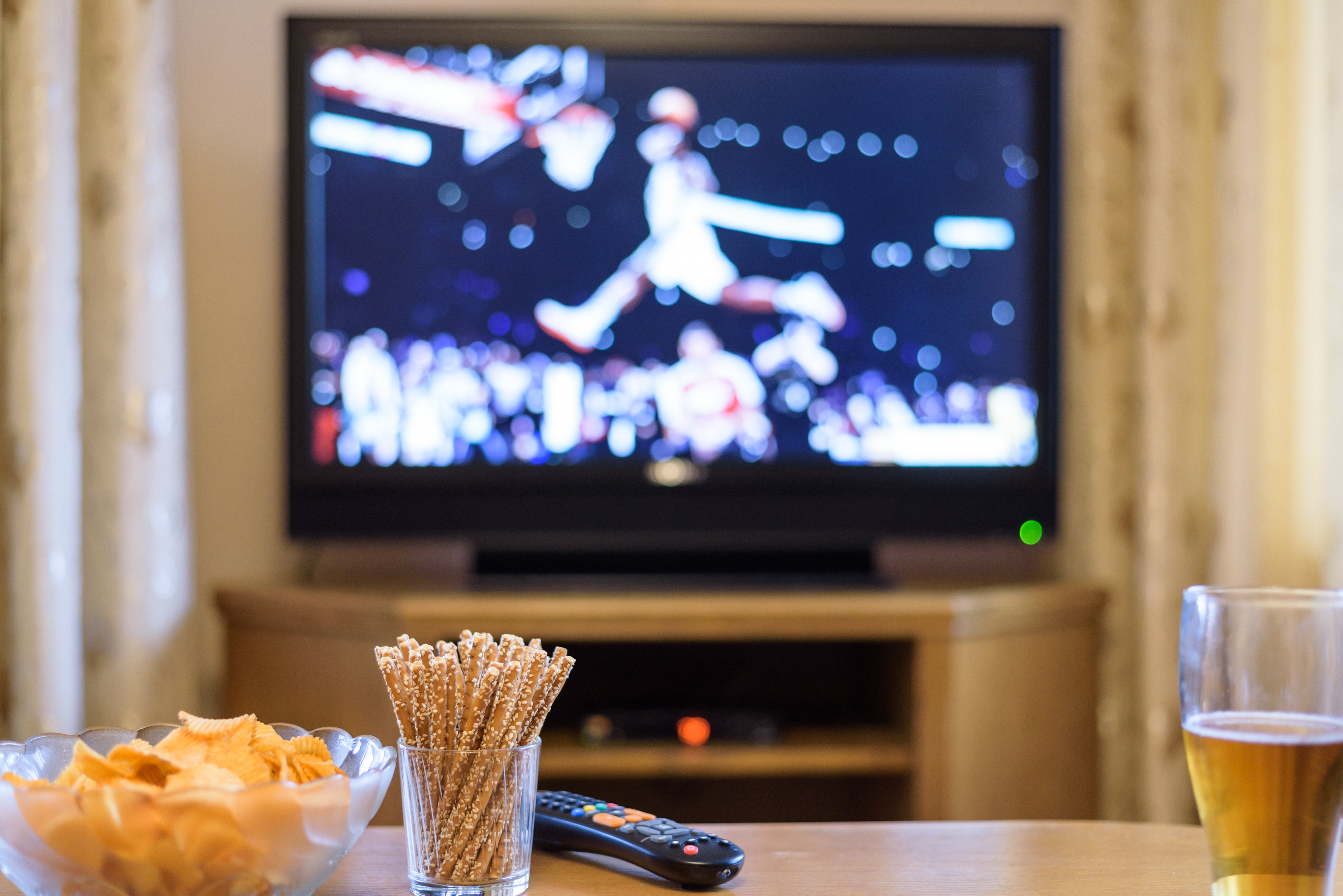 Snacks on a coffee table set against the backdrop of a basketball game on television | Source: Shutterstock