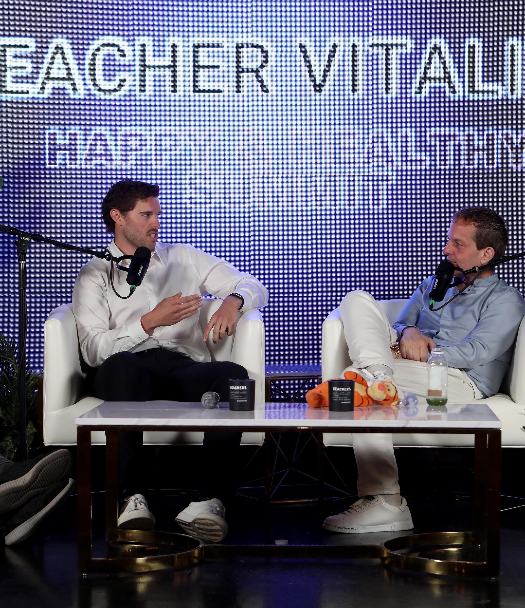 Gesturing as he speaks, Christopher Schwarzenegger actively contributes to the conversation with Jeff Beacher. The image captures his confidence and clarity as he reflects on his own journey to better health.