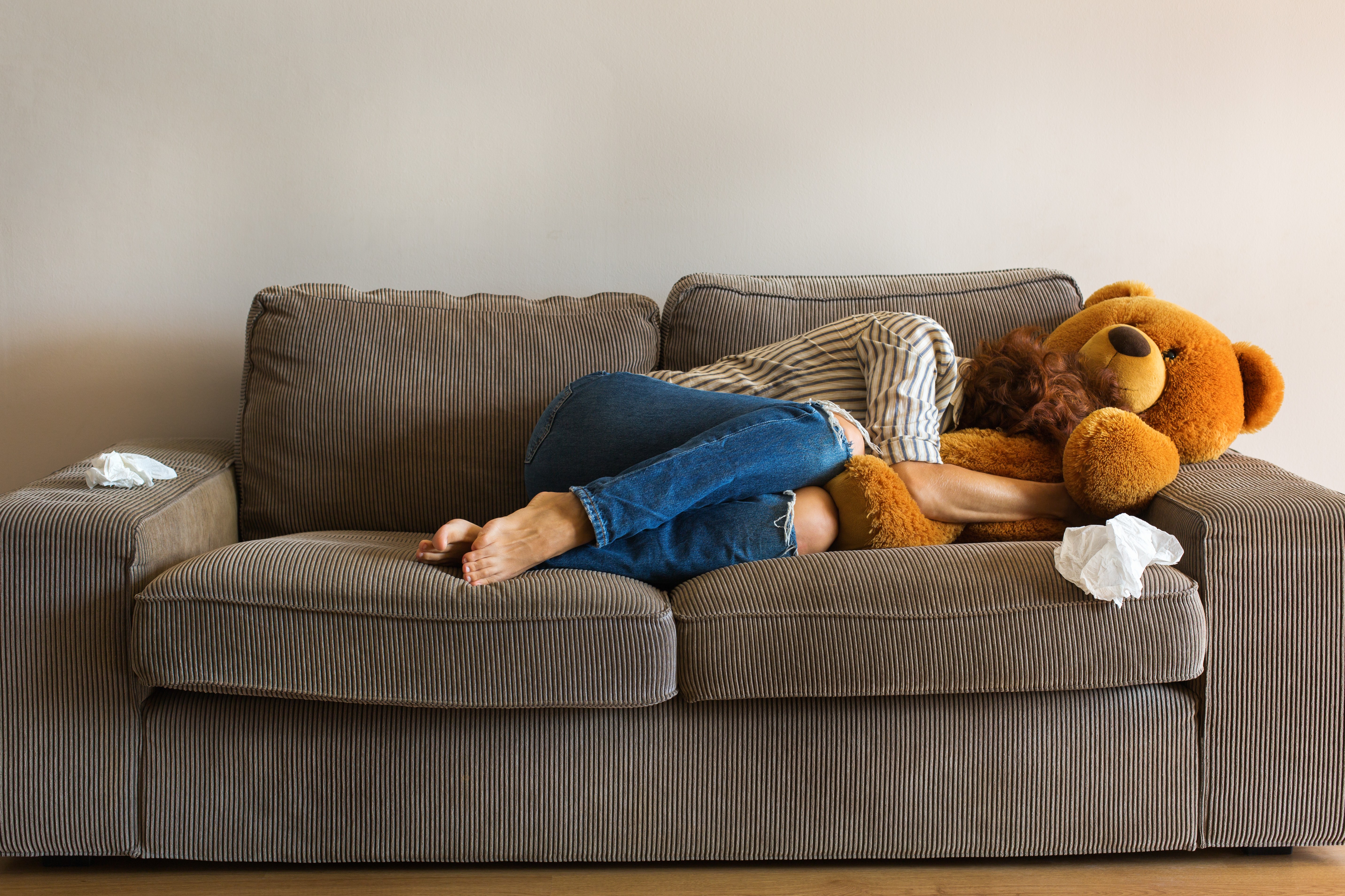 A depressed young woman lies on the couch and cries while hugging a teddy bear | Source: Shutterstock