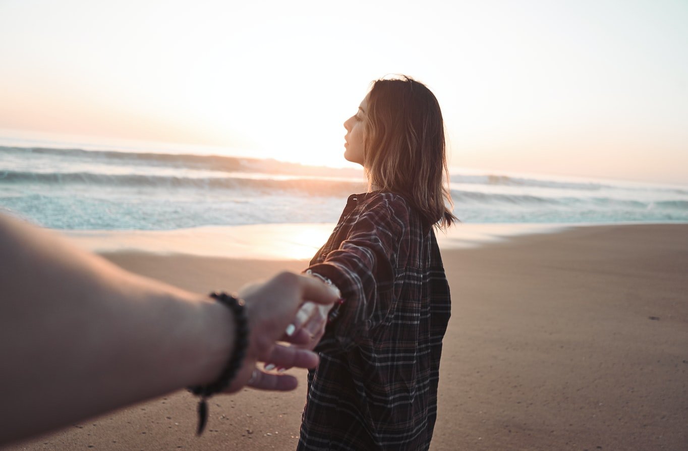 Frau und Mann halten sich an der Hand am Strand | Quelle: Unsplash