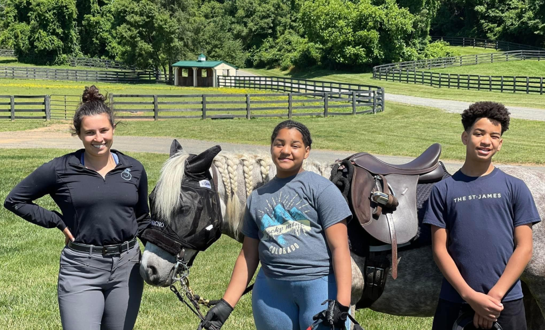 Cerina and Justin Fairfax’s children pose beside a saddled horse with a riding instructor during an outdoor outing | Source: Facebook/justin.fairfax.2025