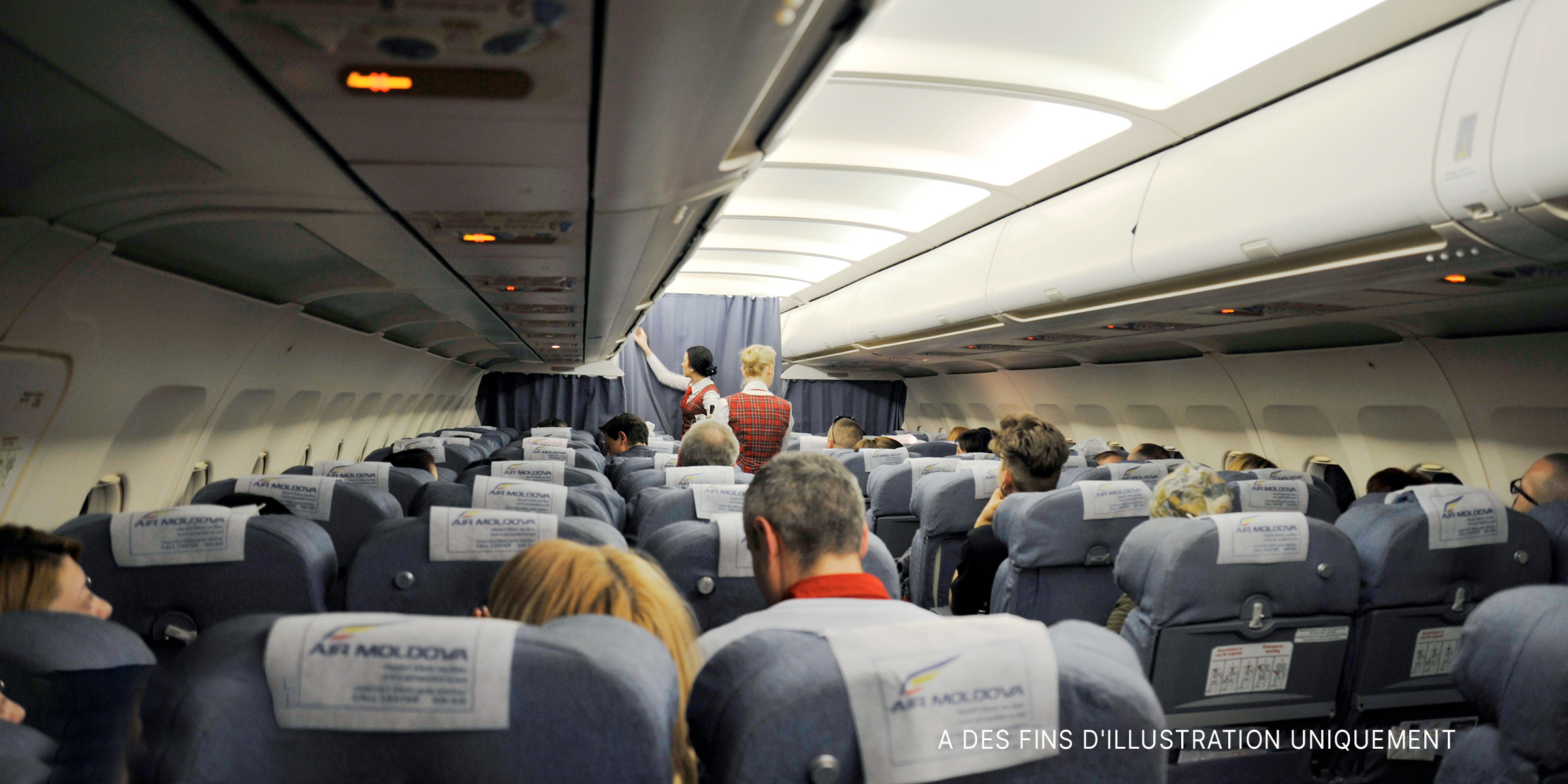 L'intérieur d'un avion avec des passagers assis et des hôtesses de l'air | Photo : Shutterstock