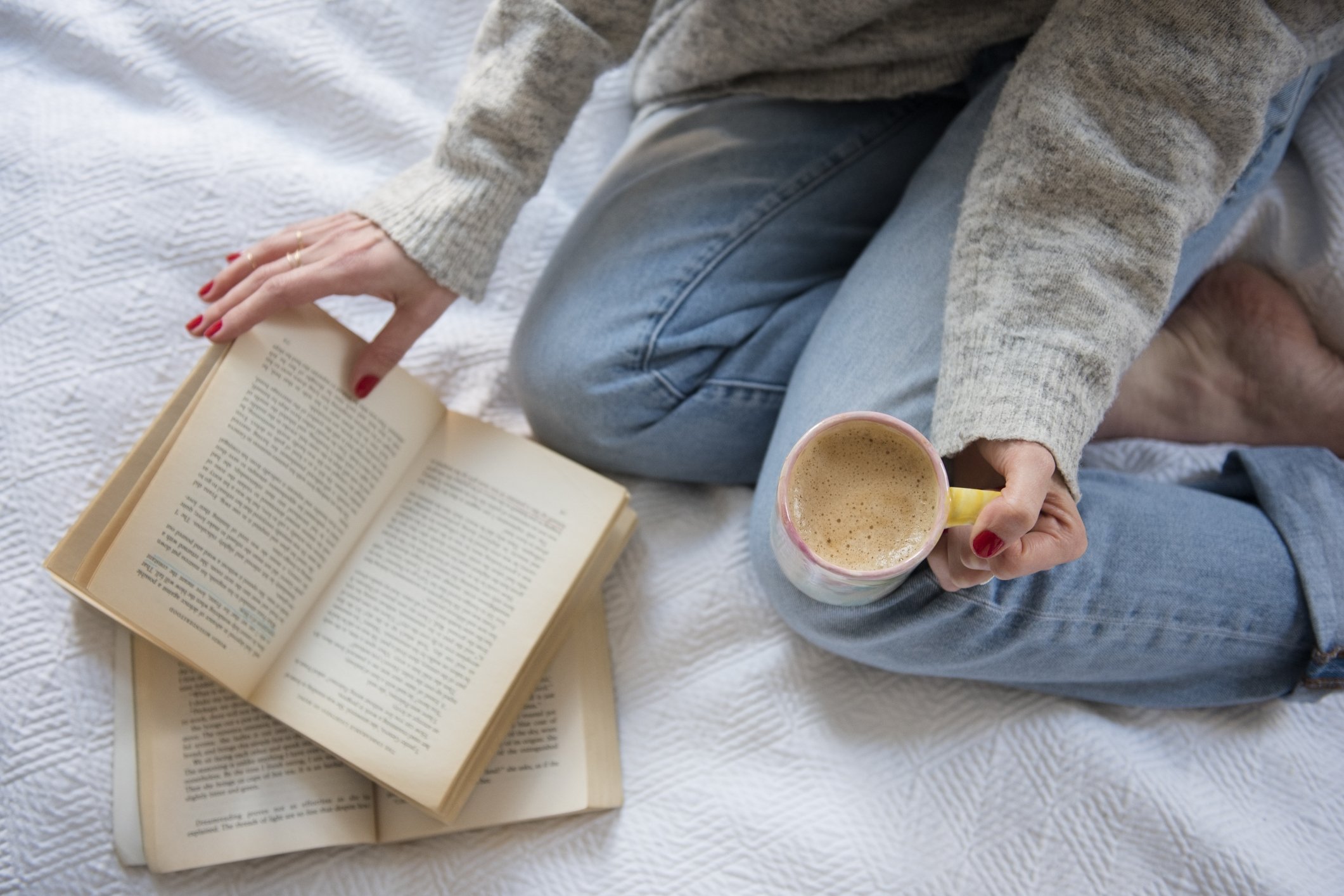 Frau im Bett mit Kaffee und Buch | Quelle: Getty Images