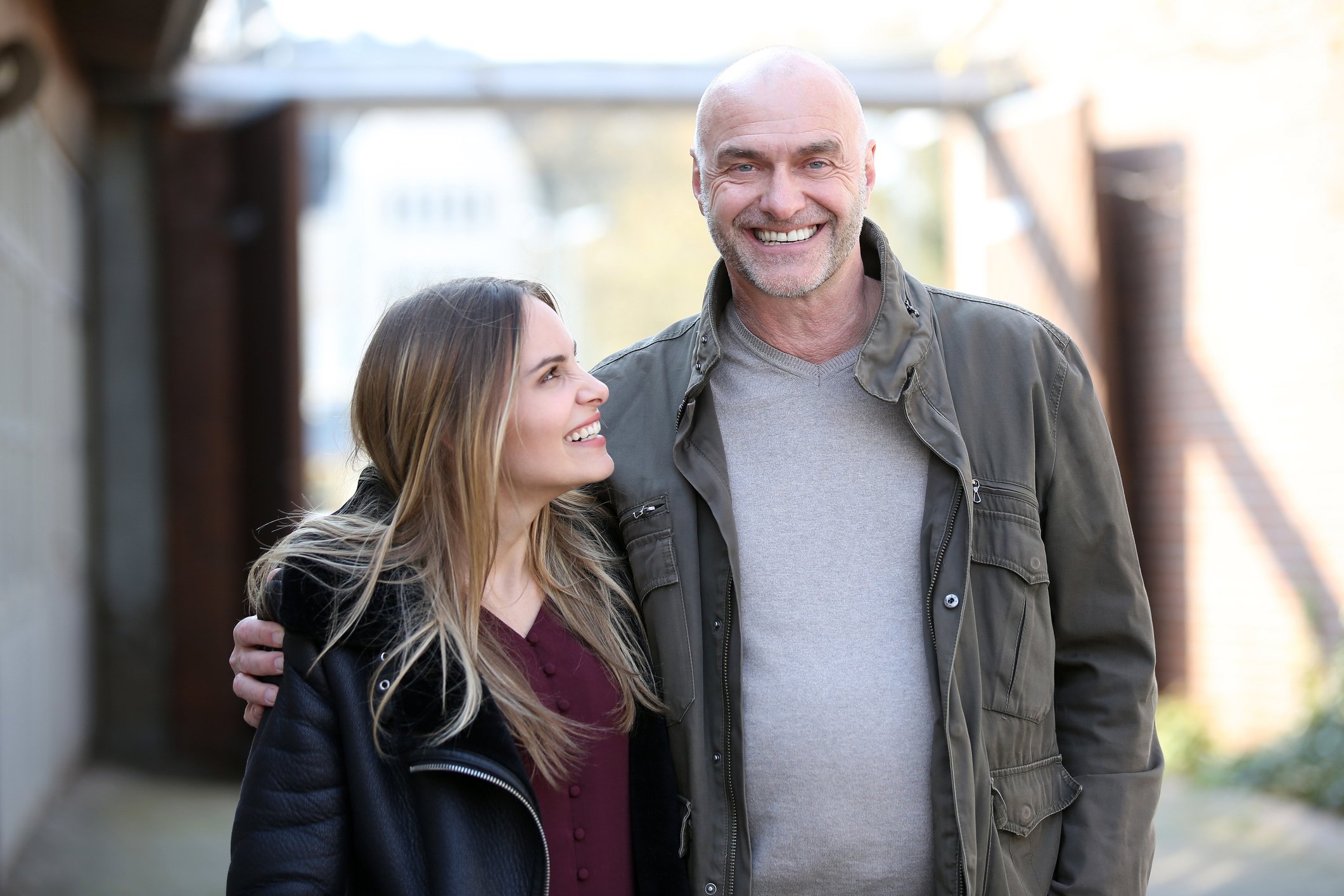 Man laughs happily into the camera while holding a younger woman in his arms | Photo: Getty Images.