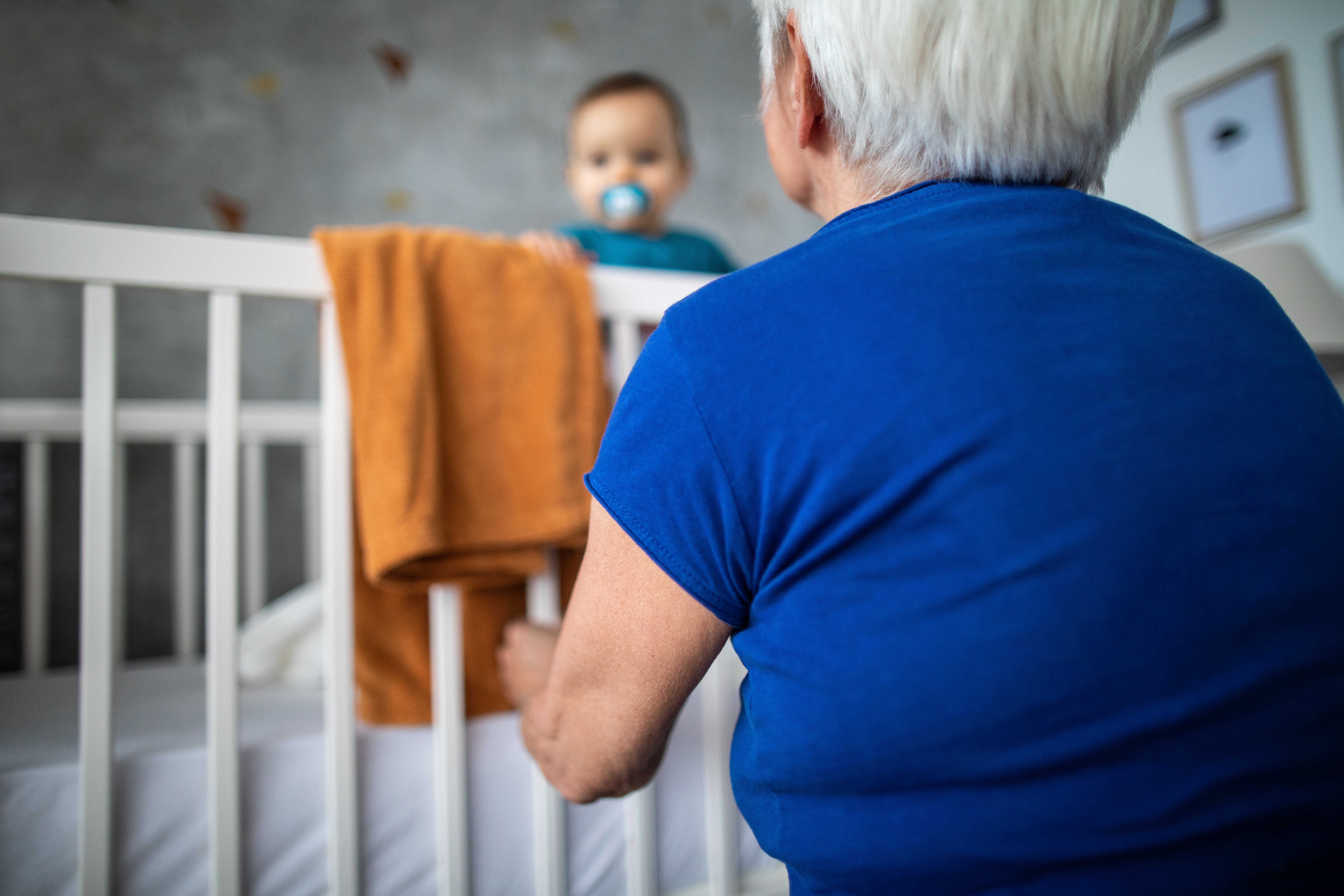 A grandmother communicating with grandson in the crib in a nursery room | Source: Getty Images