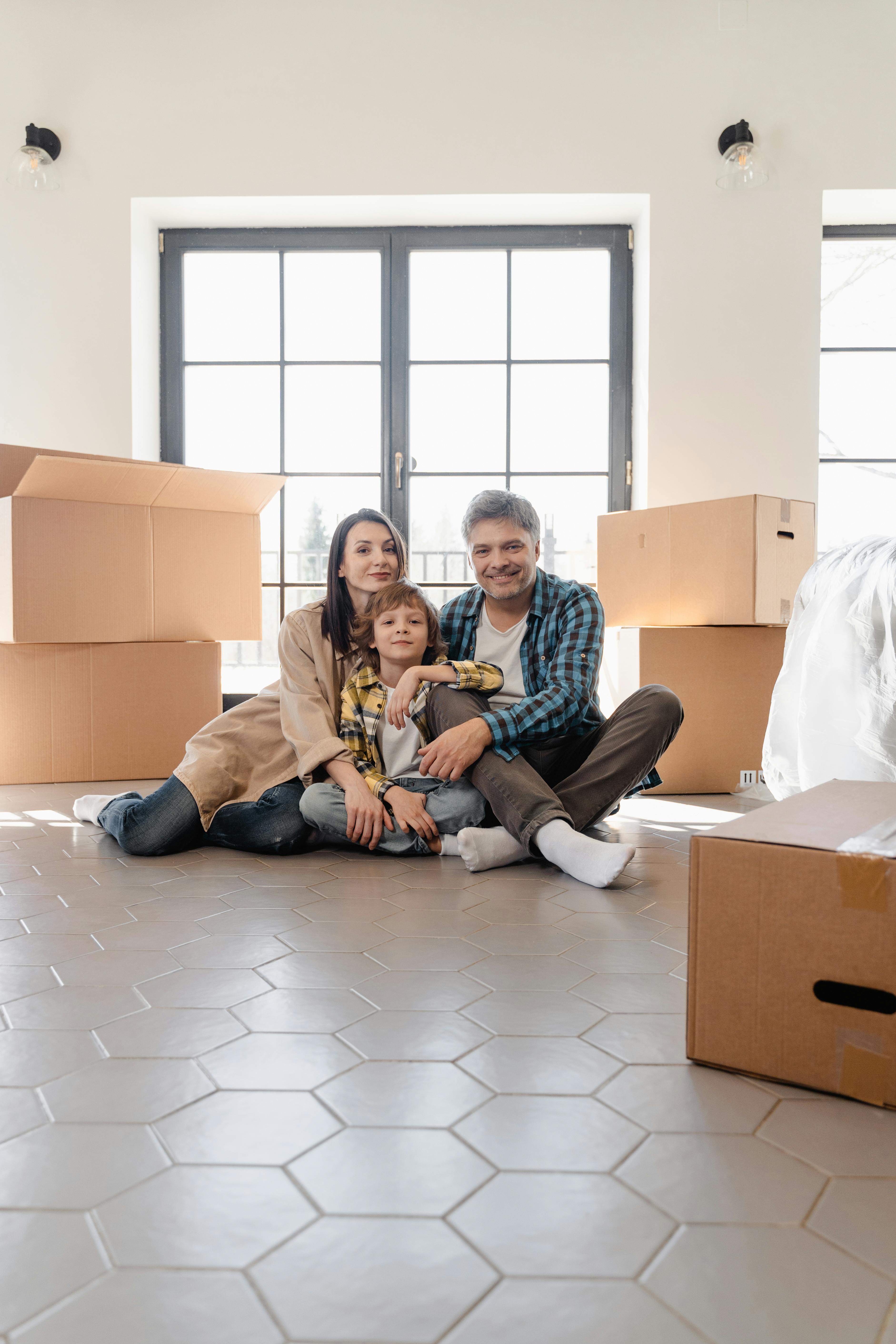 A family of three sitting on the living room floor with boxes around them | Source: Pexels