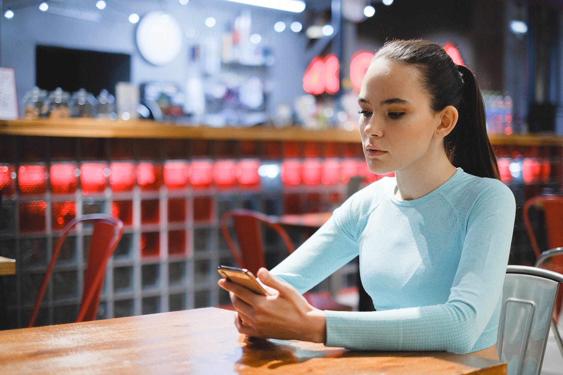 Junge Frau schaut in einem Café auf ihr Handy | Quelle: Pexels