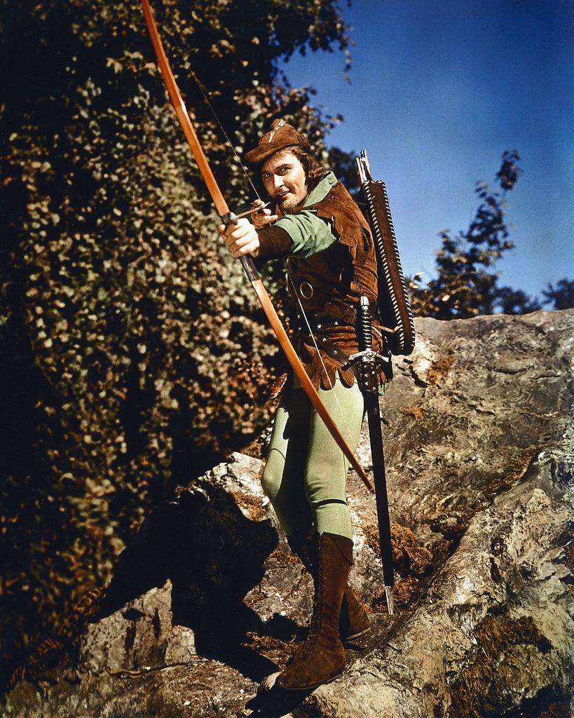  Australian actor, poses in costume, taking aim with a bow-and-arrow in a publicity portrait issued for the film, 'The Adventures of Robin Hood', USA, 1958 | Photo: Getty Images