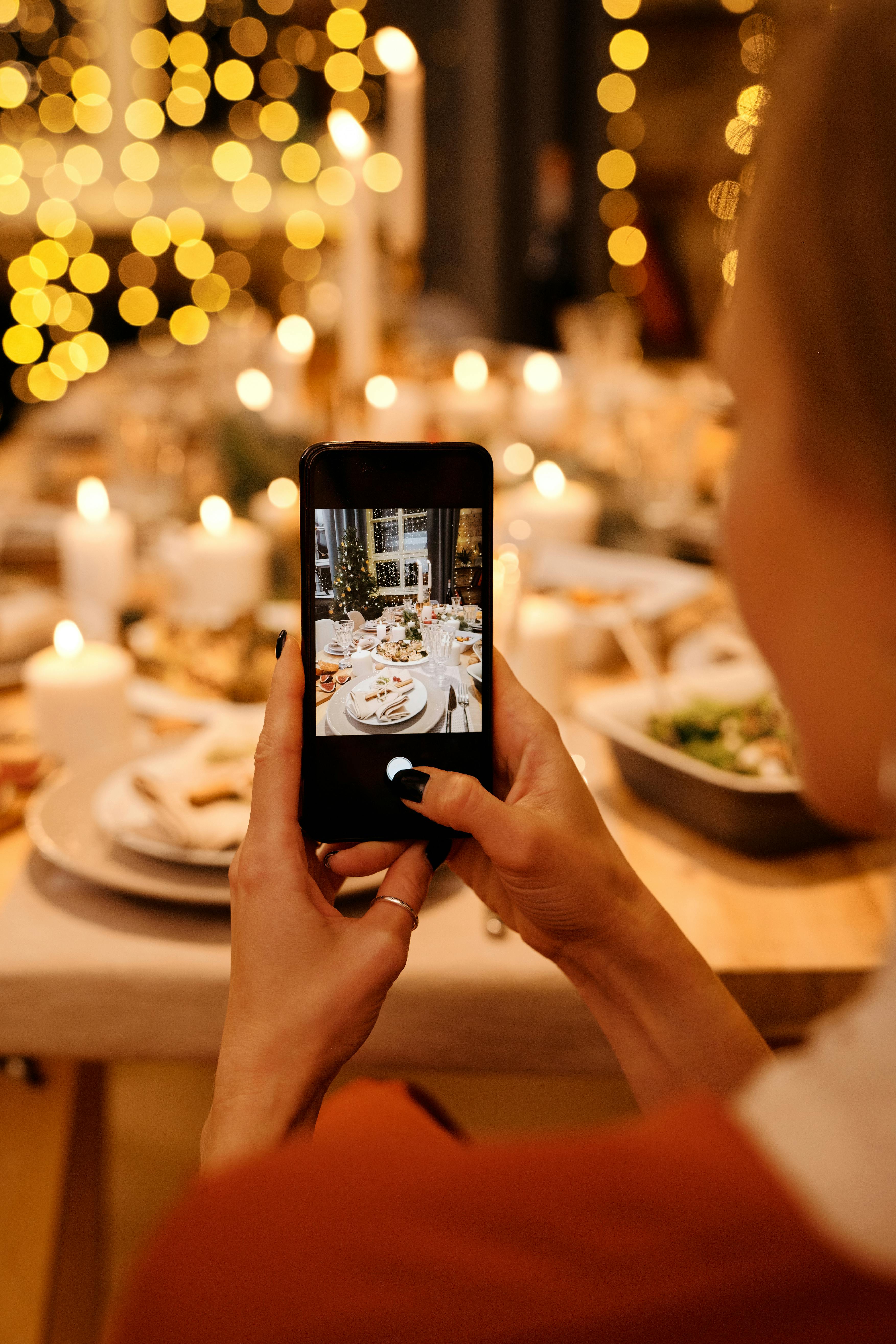 A hand holding a cellphone and taking a photo of a dinner setting | Source: Pexels