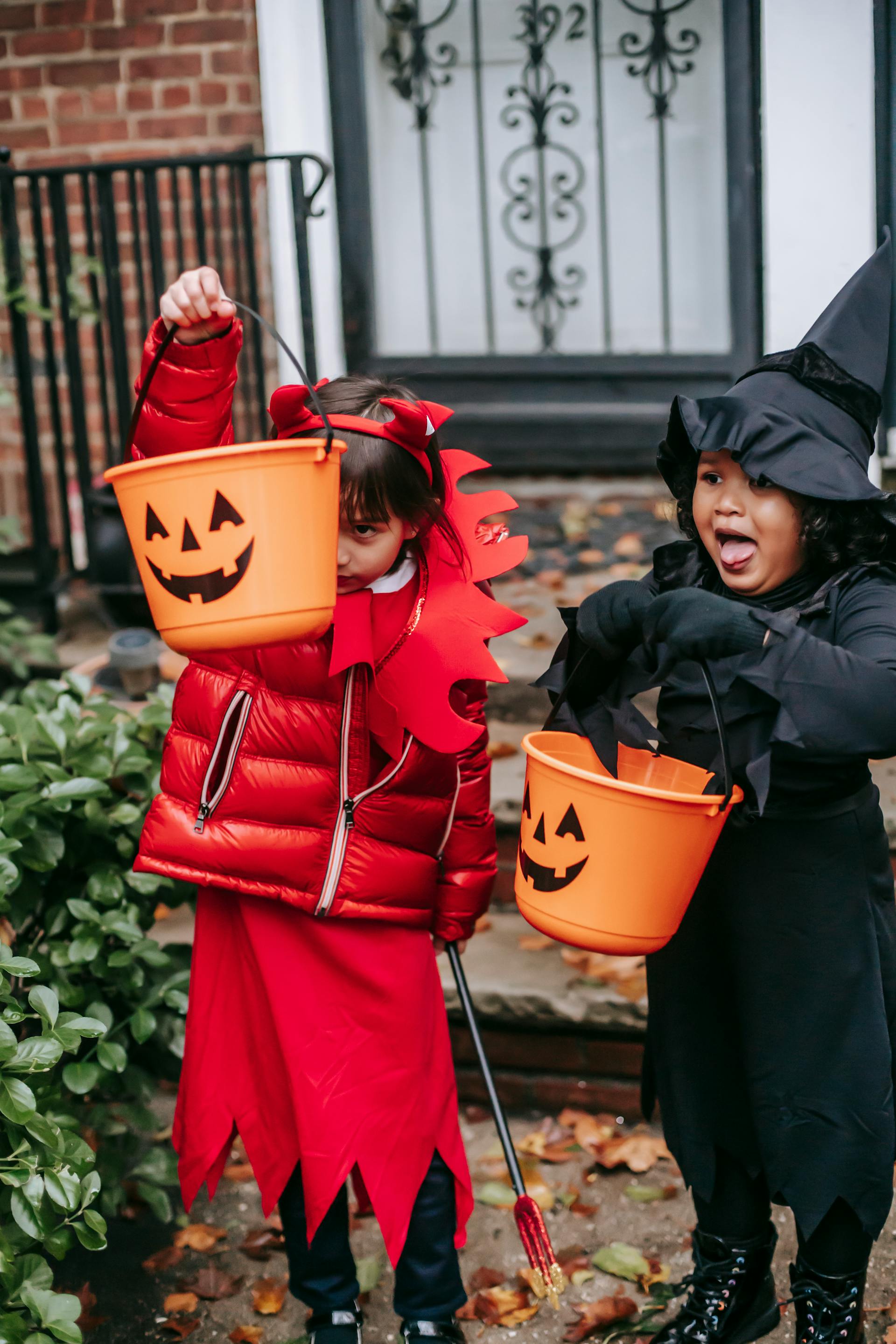 Kids trick or treating in Halloween costumer near a house entrance | Source: Pexels