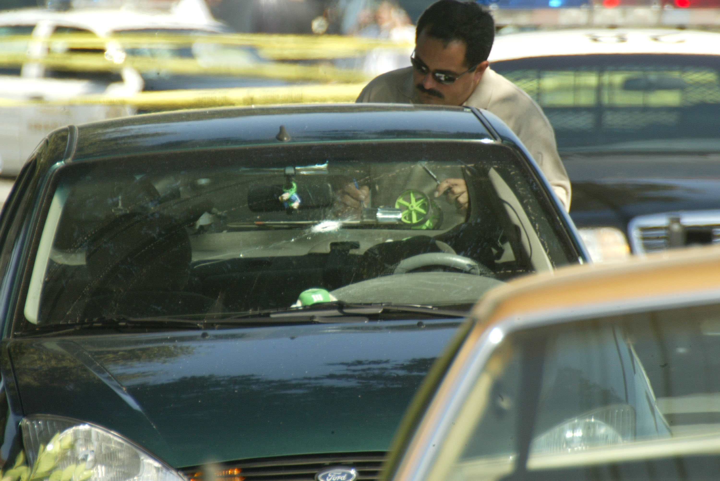 A Los Angeles Police forensic officer examining a shot-out car at the crime scene where 31-year-old Yetunde Price was fatally shot on September 14, 2003, in Compton, California. | Source: Getty Images