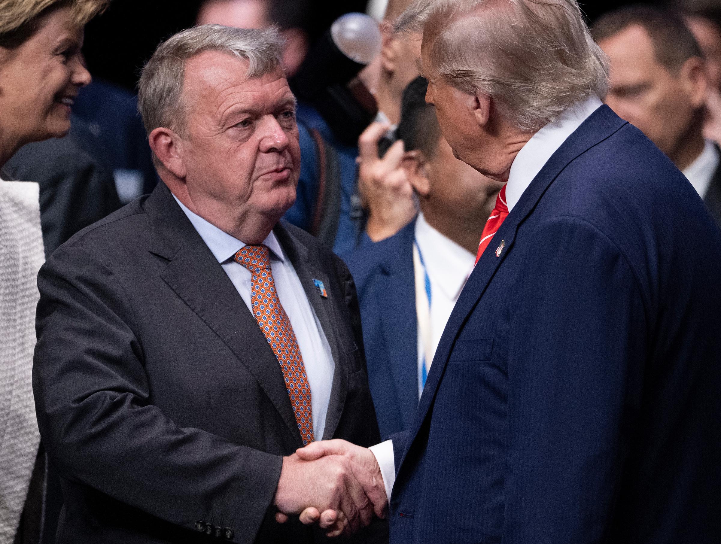 Denmark's Foreign Minister Lars Løkke Rasmussen and Trump share a firm handshake, their eyes locked in a moment of mutual focus. The two appear engaged in a thoughtful conversation, underscoring the diplomatic tone of the summit.
