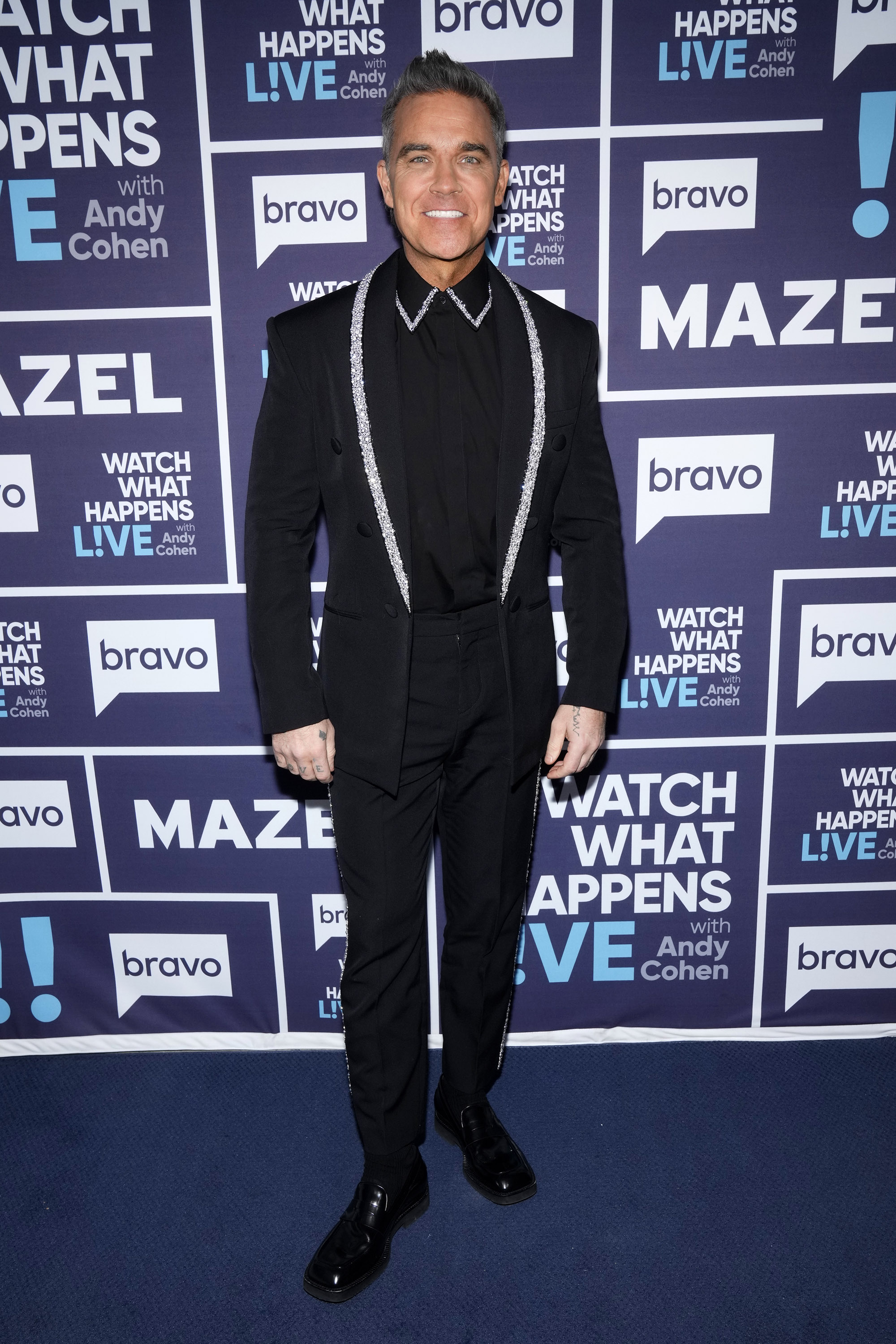 Robbie Williams appeared on "Watch What Happens Live With Andy Cohen" in 2025, dressed in a sleek black suit with glittering trim. Flashing a smile on the press line, he blended sharp style with his ever-charismatic presence.