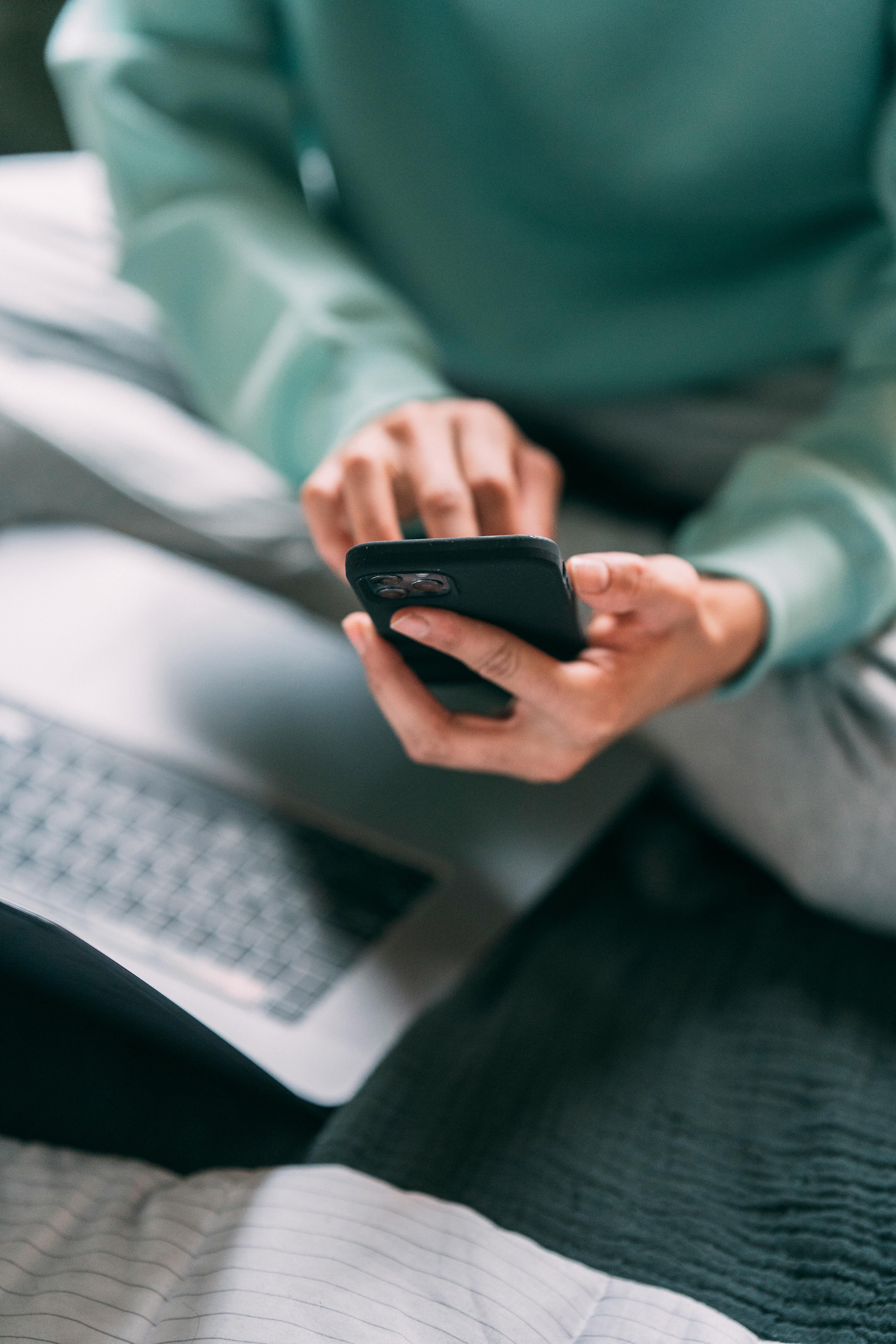 Someone using their phone with a laptop open in front | Source: Pexels