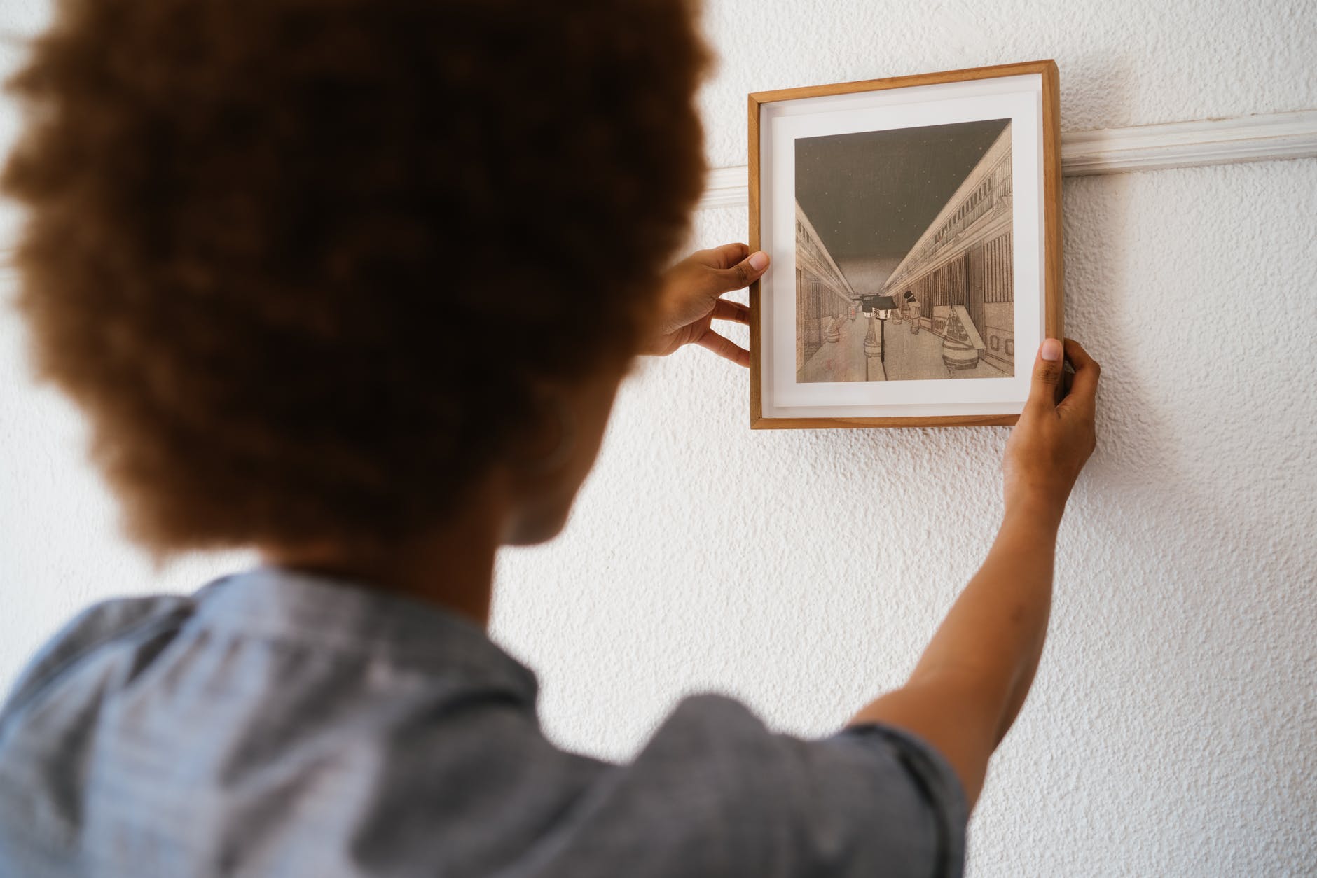 A woman hanging a framed picture on the wall. | Photo: Pexels