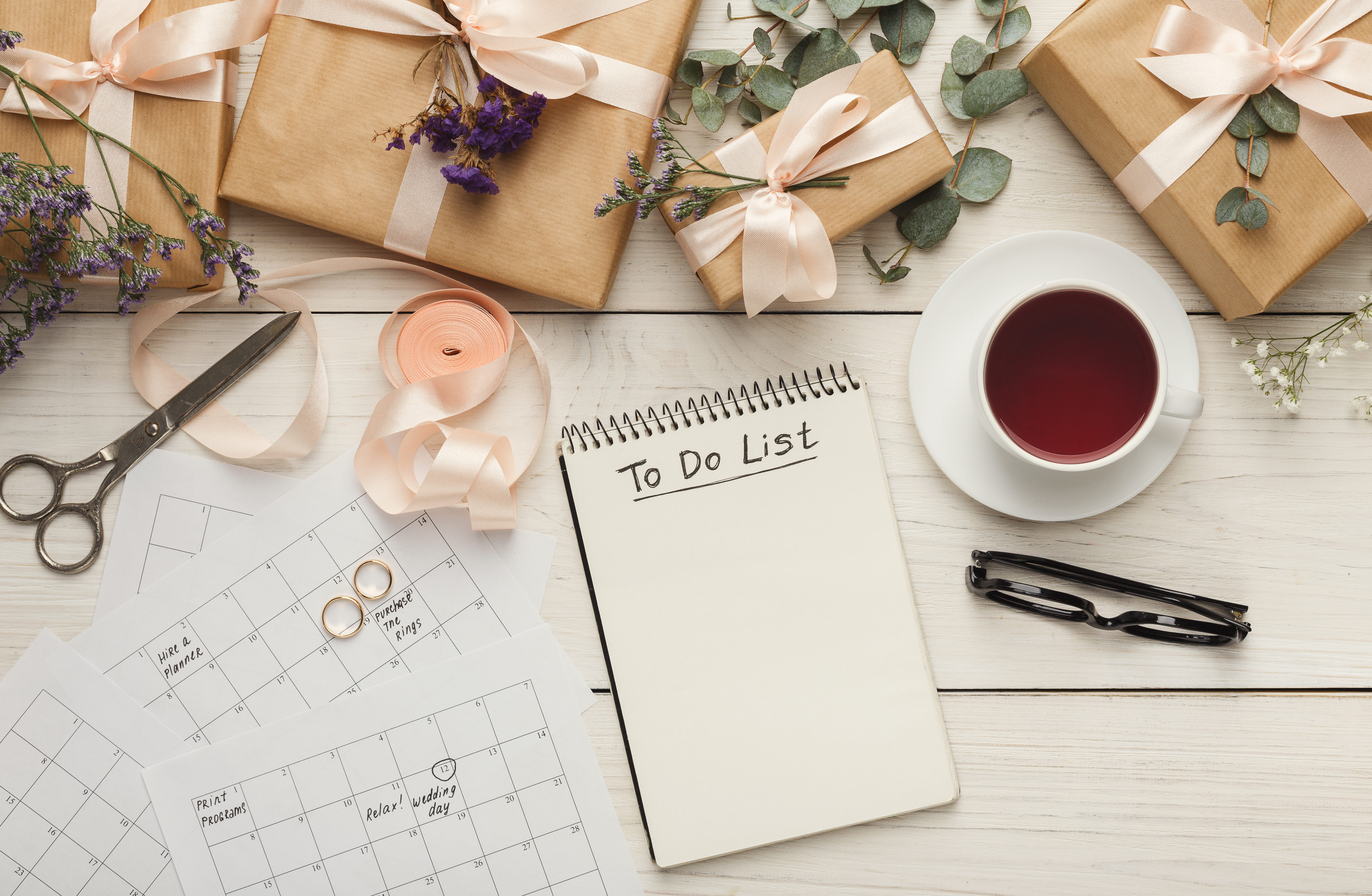 Papers and wedding paraphernalia scattered on a table, along with a cup of coffee, a pair of eyeglasses, and a notebook with the words "To Do List" scribbled on the first page | Source: Shutterstock