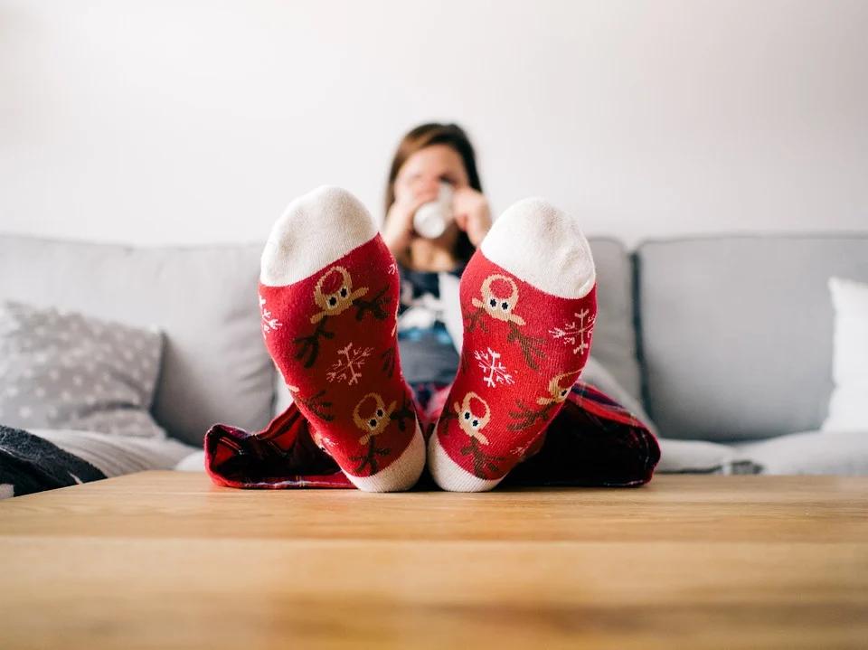 A woman sipping her hot chocolate drink while on the couch with Christmas socks on. | Photo: Pixabay