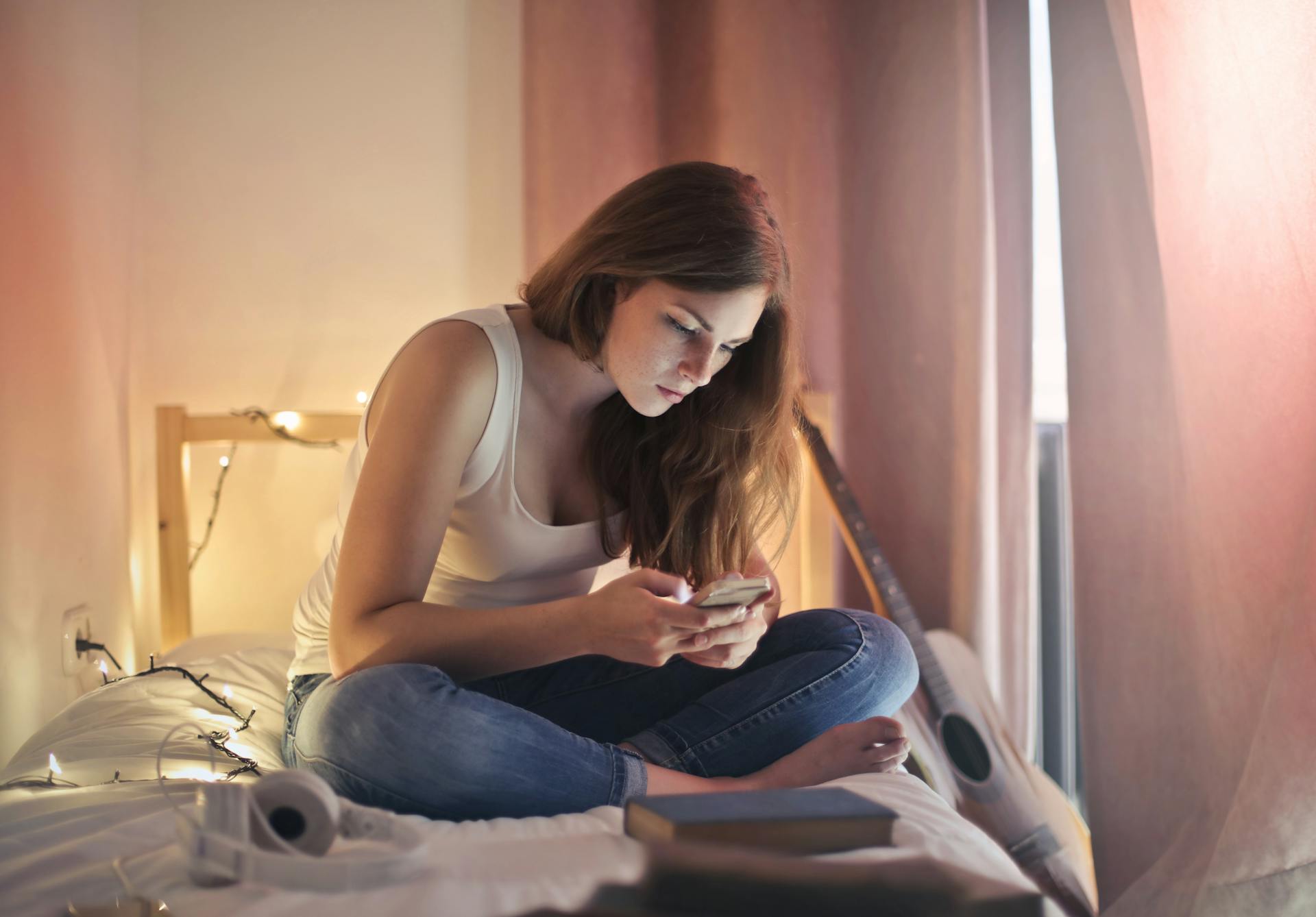 A woman using her phone while sitting on her bed | Source: Pexels