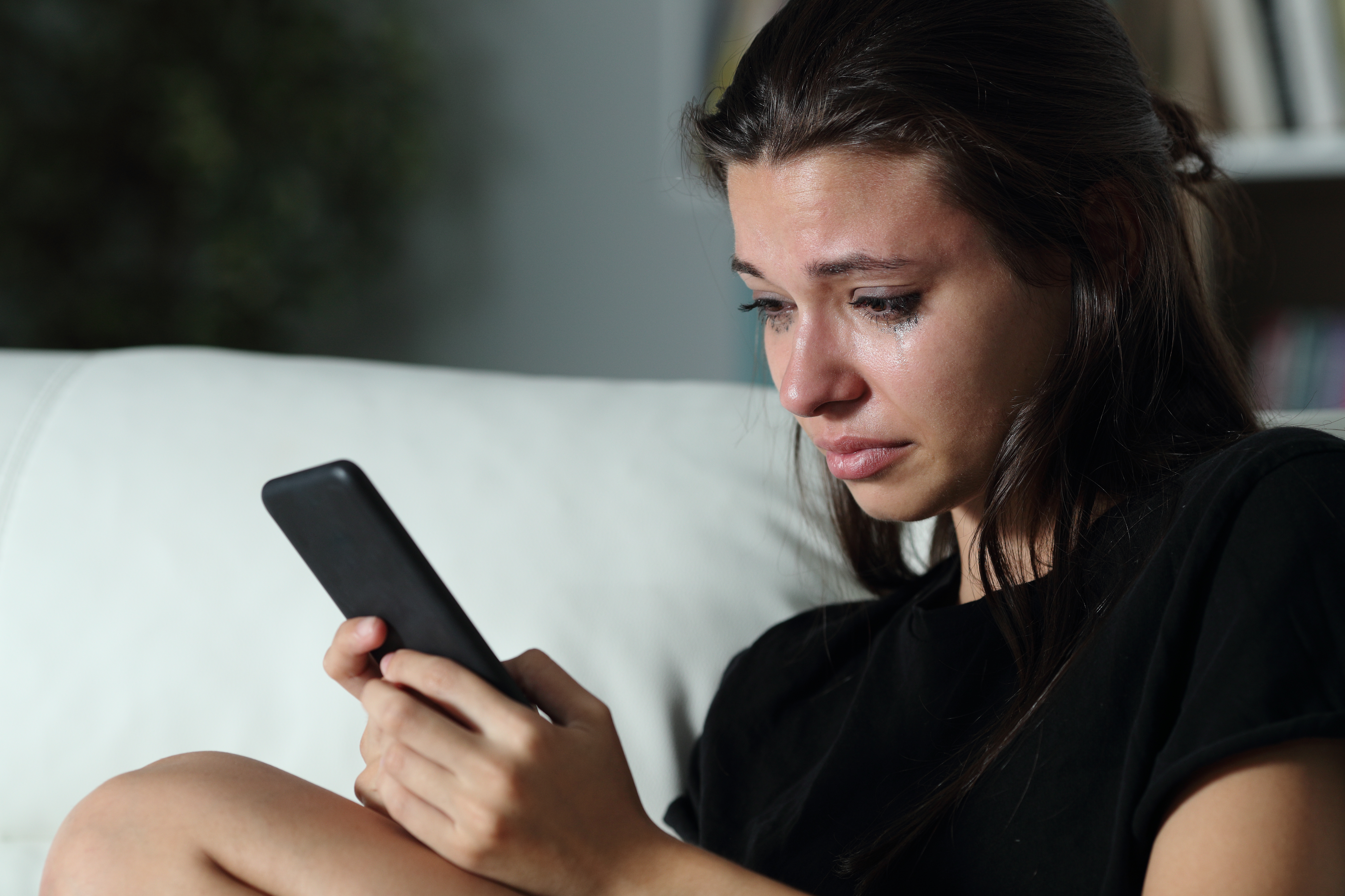 A teary-eyed young girl is pictured looking at her cell phone. | Source: Shutterstock