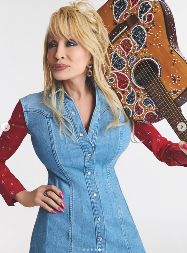 Dolly Parton poses in a fitted denim dress with a guitar | Source: Instagram/dollyparton