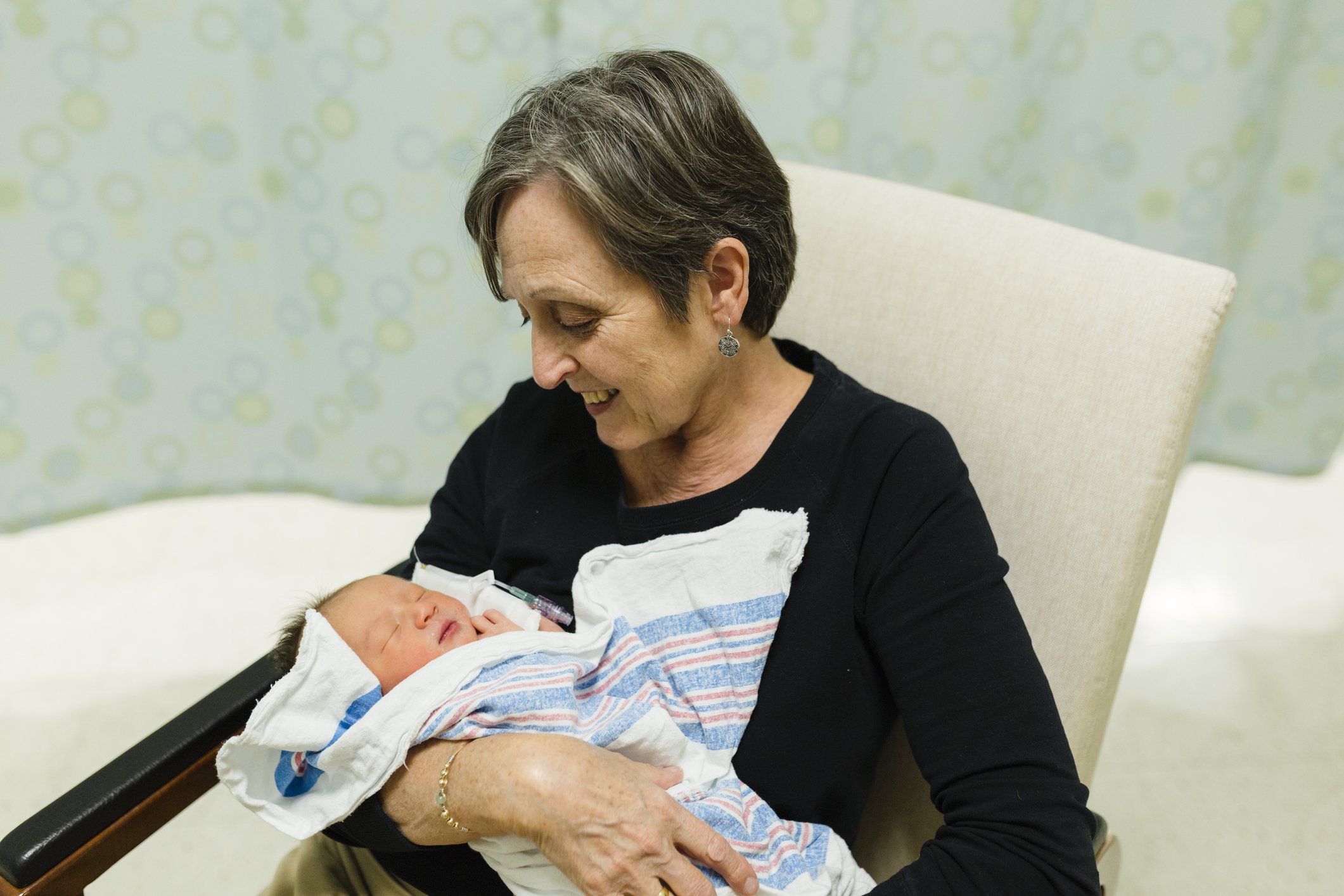 Grandmother looks down smiling at newborn grandchild in the hospital room. | Photo: Getty Images