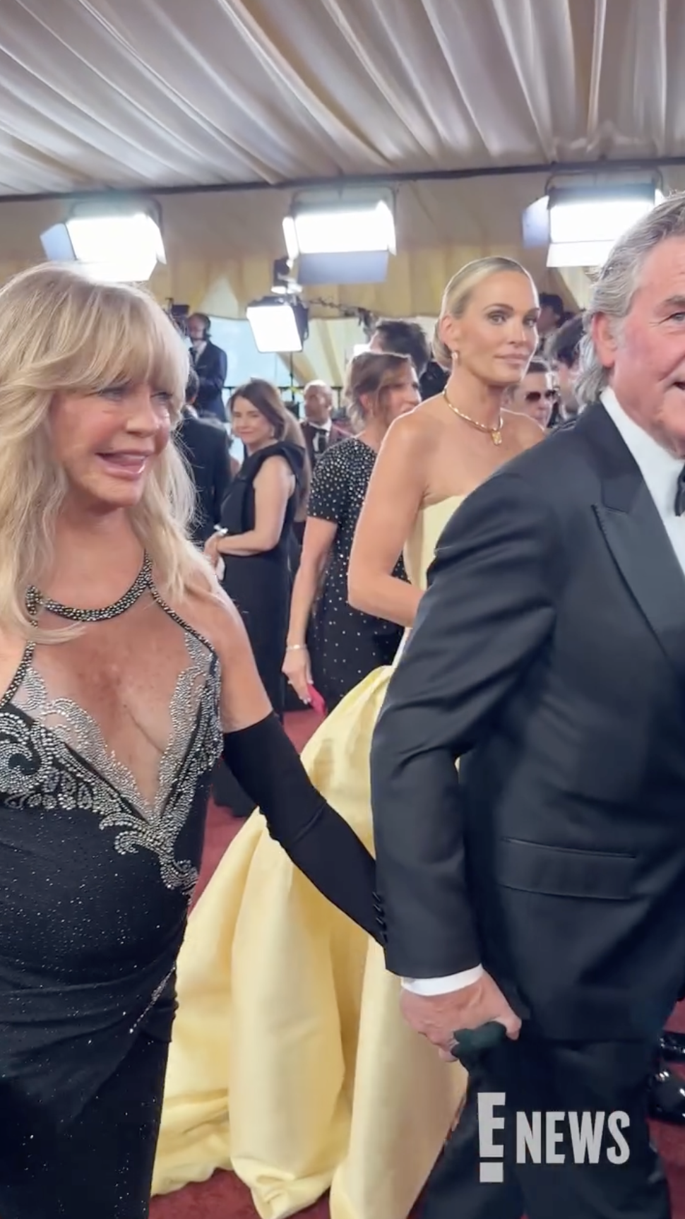 Goldie Hawn and Kurt Russell walk hand in hand through the arrivals area as other guests and photographers gather under the bright red carpet lights. | Source: Instagram/enews