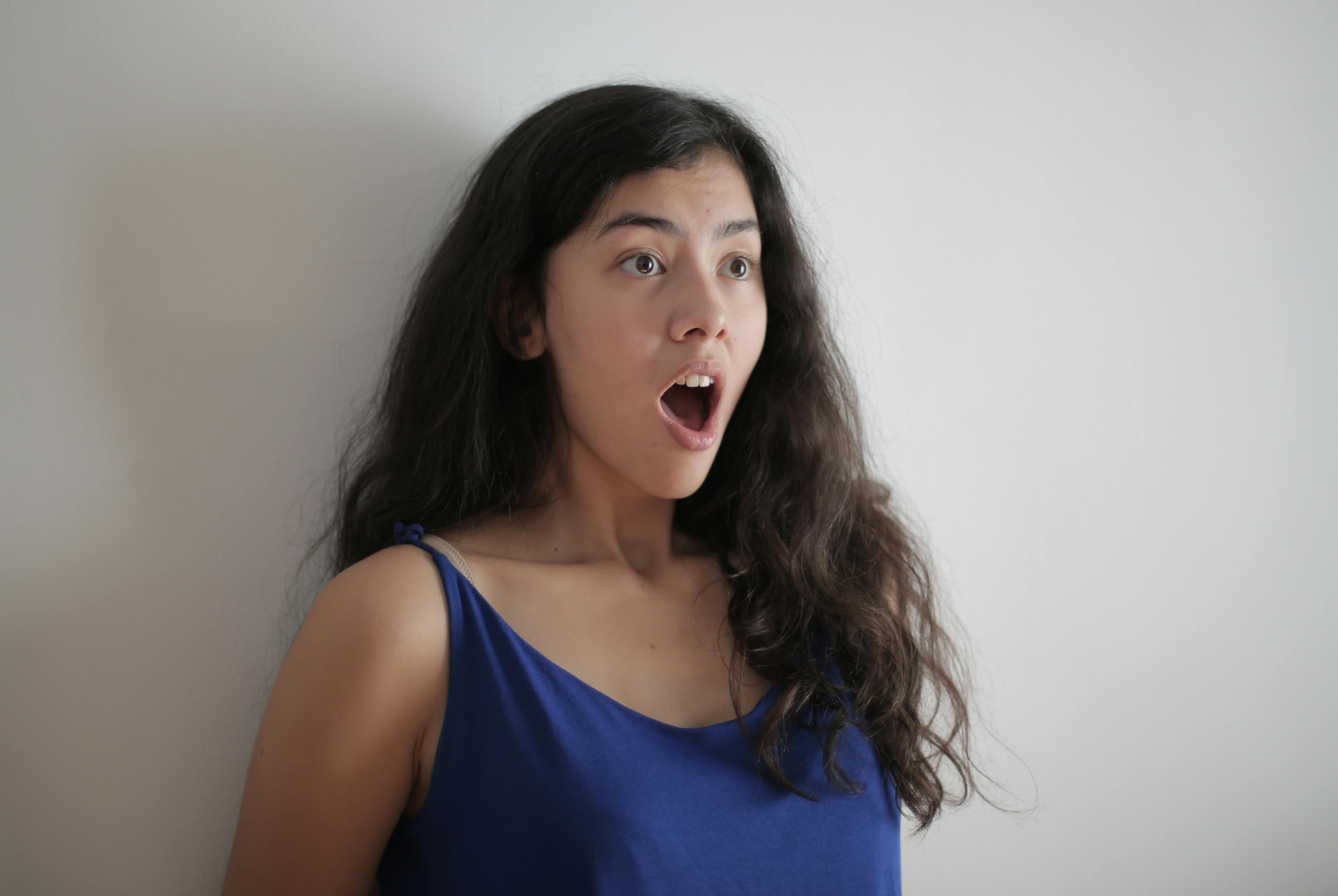 A shocked woman with her mouth open standing against a wall | Source: Pexels