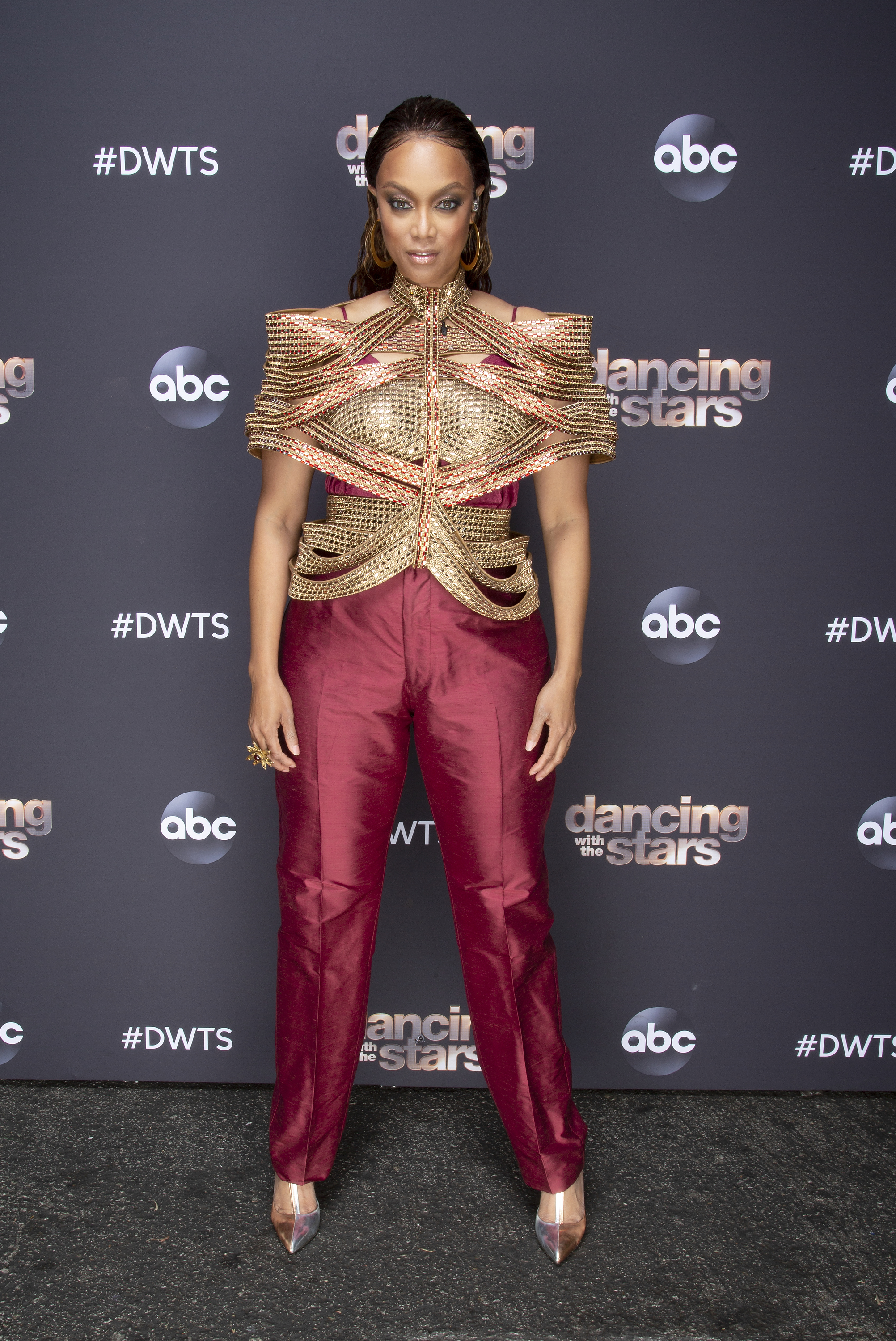 Tyra Banks stood out on "Dancing with the Stars" in a gold sculpted top and burgundy satin trousers. Sleek hair, bold eye makeup, and gold heels finished her bold, futuristic look.