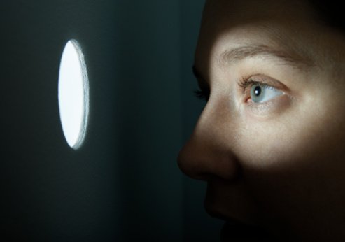 Woman looking through illuminated peep hole.| Photo: Getty Images