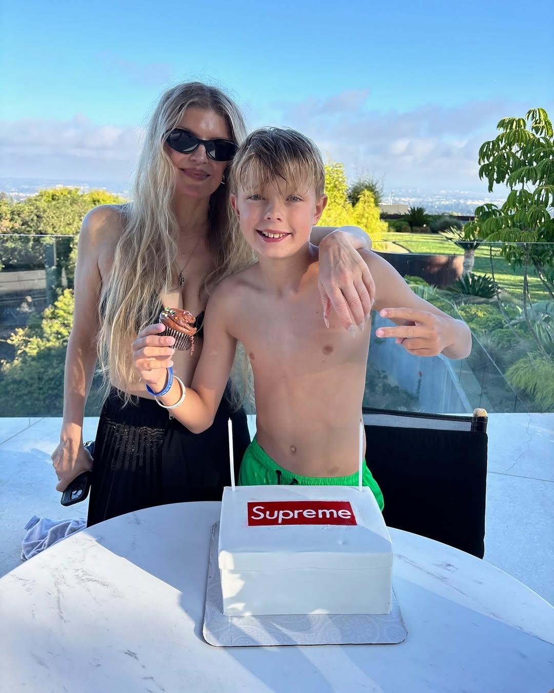 Fergie and her son Axl Duhamel dressed in bathing suits, posing with a cake, from her birthday tribute posted on August 29, 2025 | Source: Instagram/fergie