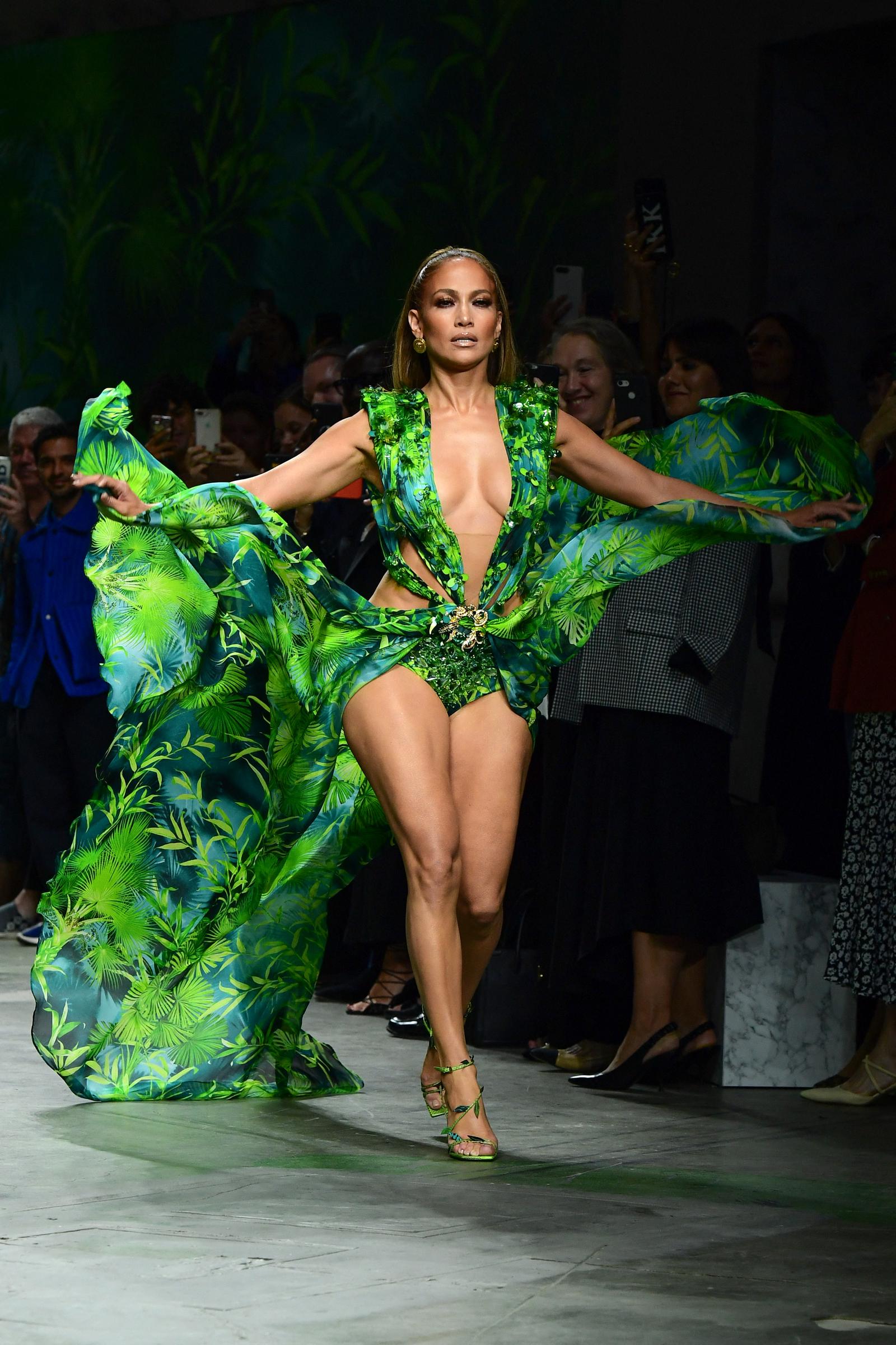 Lopez revisited the tropical-print Versace look from 2000, wearing an updated version on the Milan runway nearly 20 years after the original Grammy Awards appearance. She completed the look with sleek, center-parted hair, bronzed makeup, and strappy green heels, emphasizing the dramatic silhouette of the design.