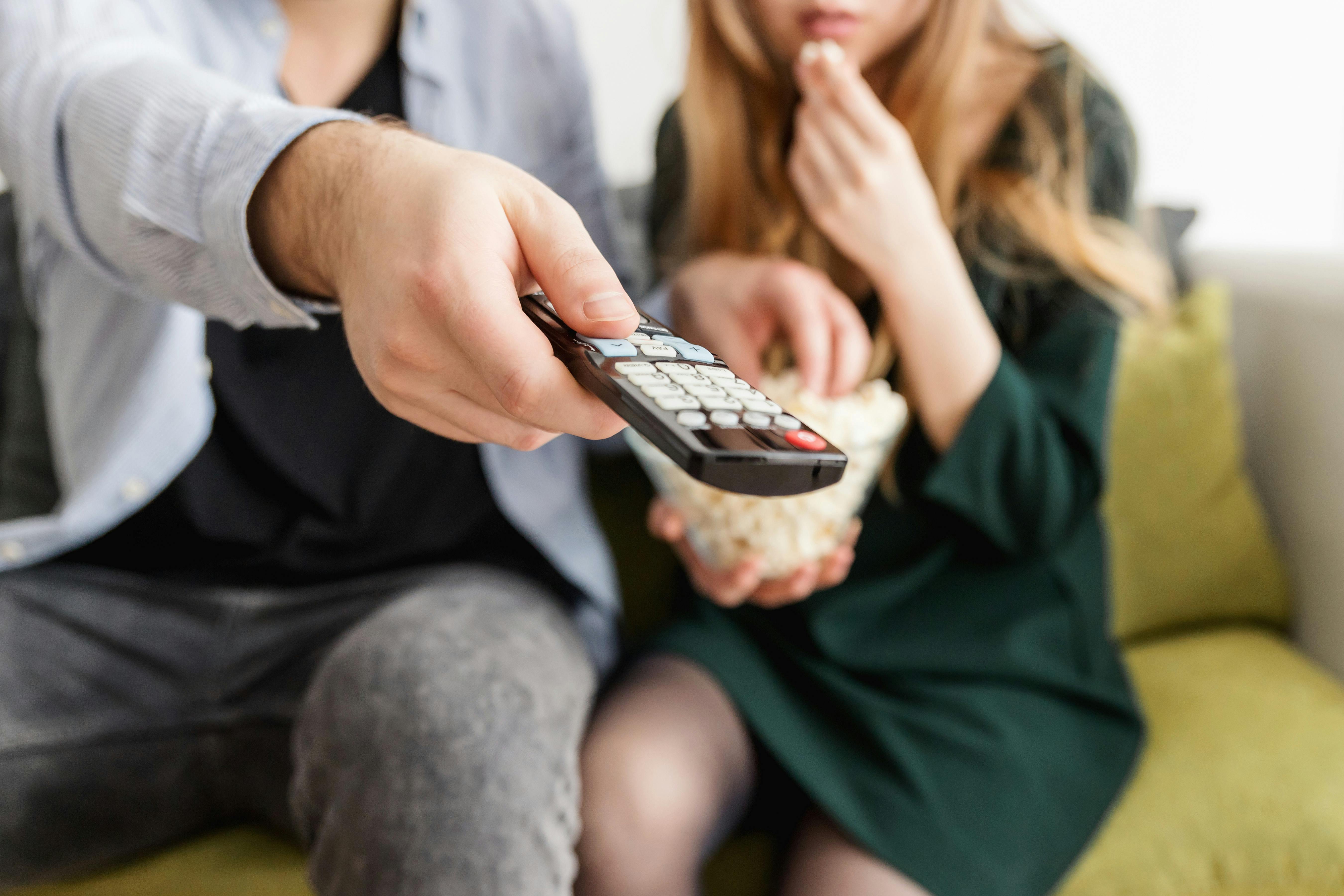 A man operates a remote control, sitting next to a woman on a sofa | Source: Pexels