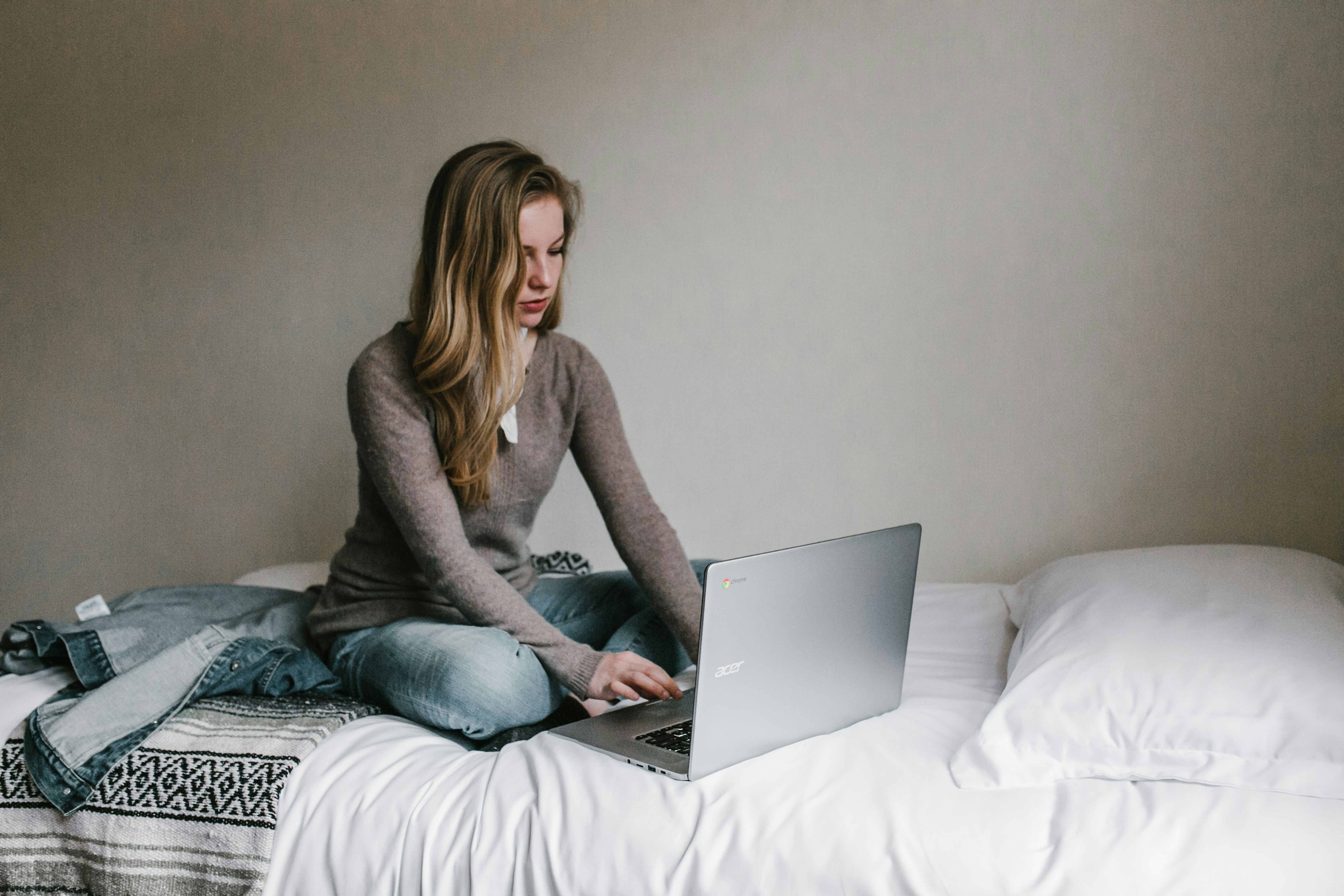 A woman working on a laptop while sitting on a bed | Source: Unsplash