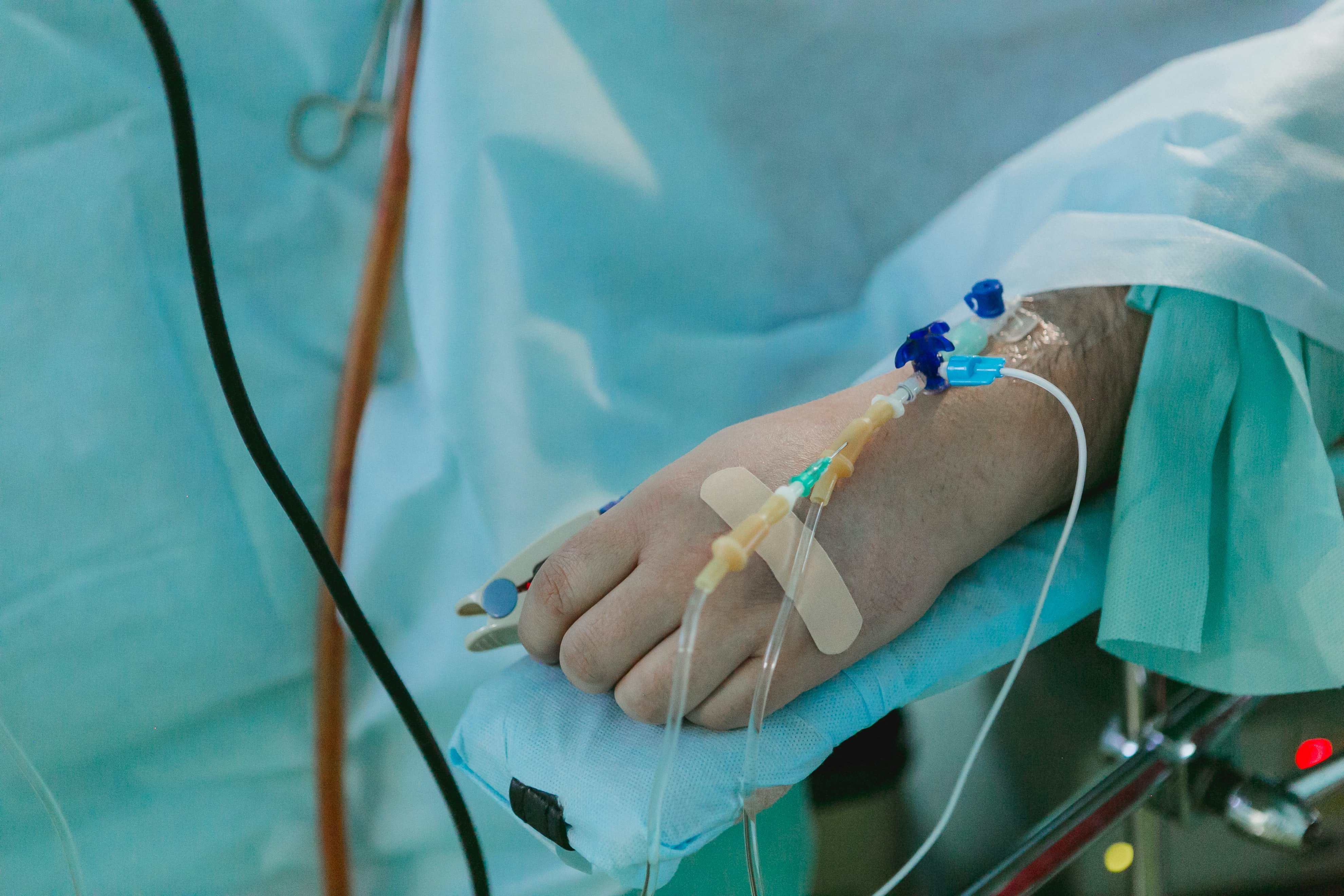 Mano de una persona en una cama de hospital con via intravenosa. | Foto: Unsplash