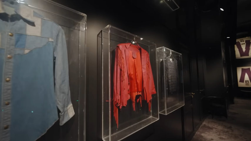 Legendary garments showcased in clear acrylic shadow boxes, including a vibrant red fringed leather jacket once owned by jazz legend Miles Davis. | Source: YouTube/@Archdigest