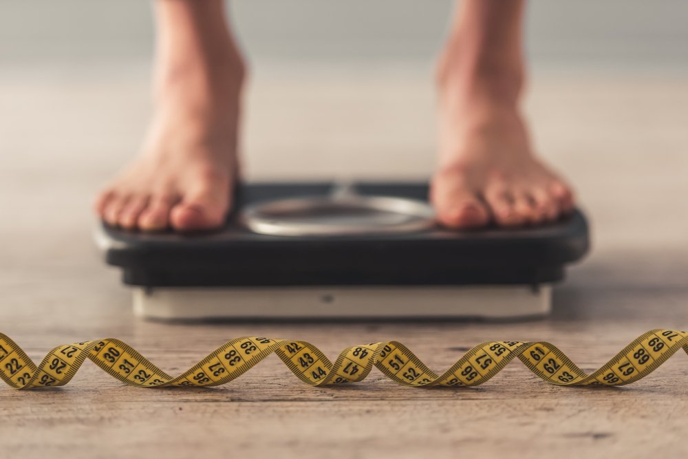 Persona midiendo su peso sobre una balanza con una cinta métrica en frente. | Foto: Shutterstock