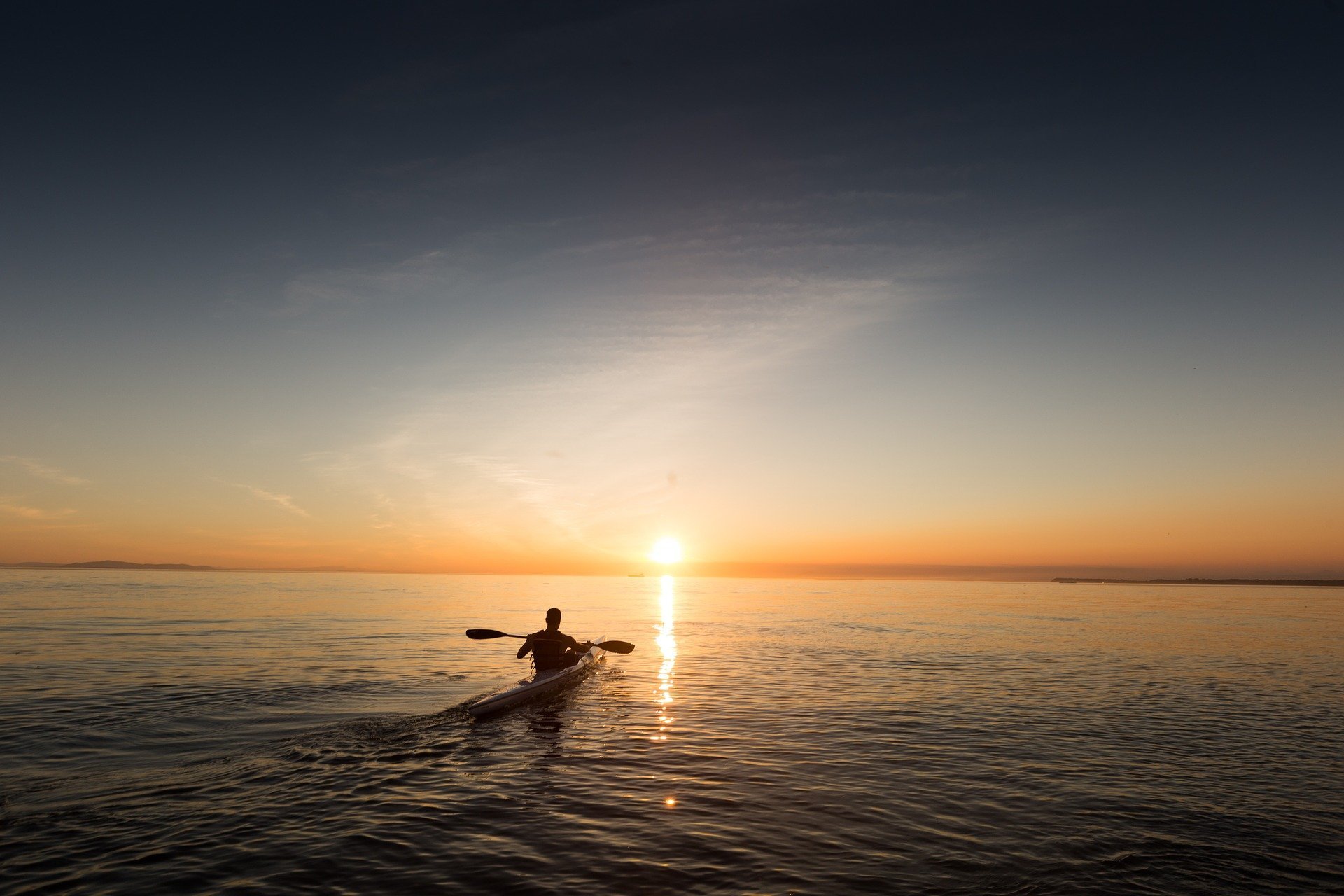 A silhouette of a person kayaking while the sun sets in front of him in the ocean | Photo: Pixabay/Free-Photos