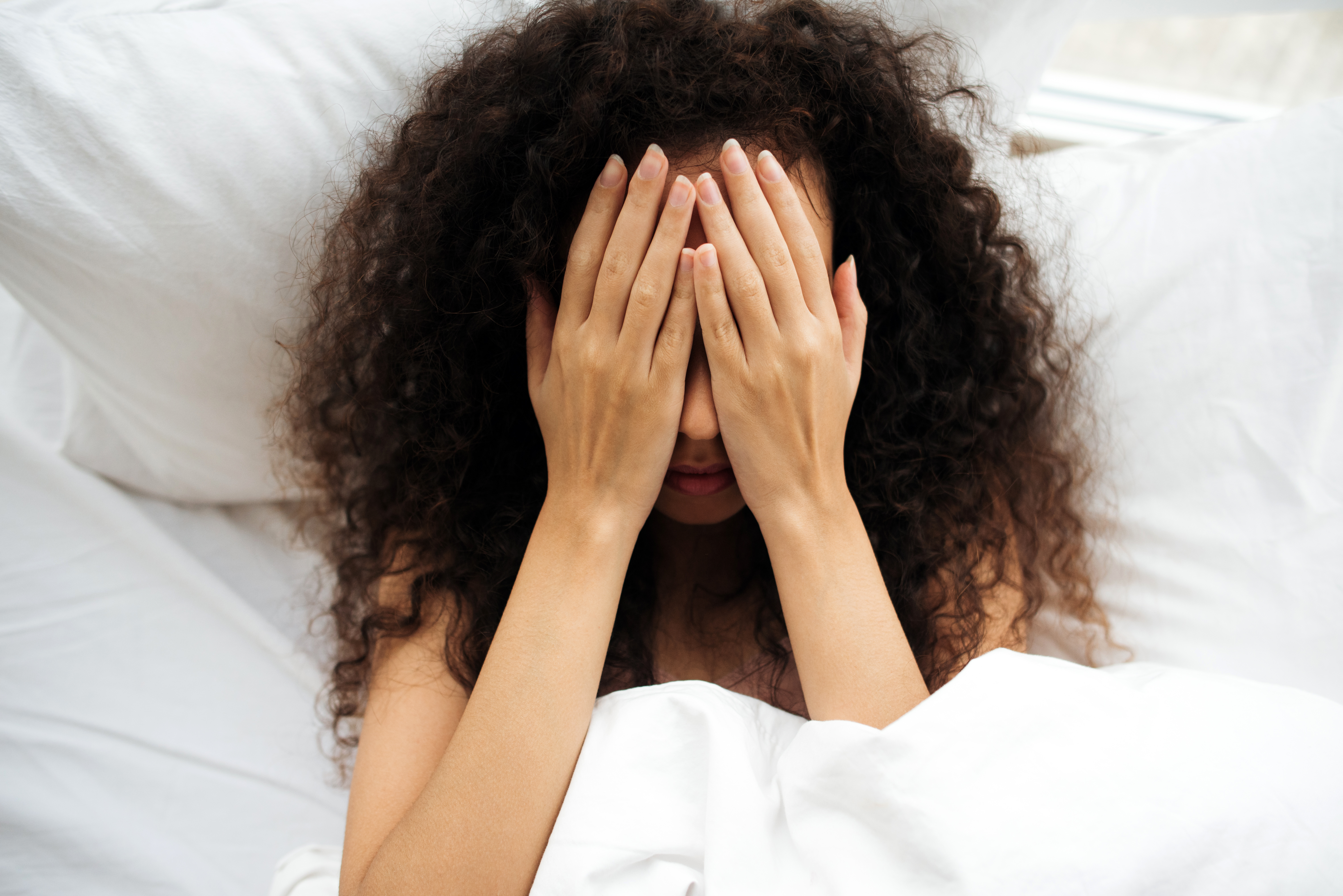 Woman in bed covering her face with her hands | Source: Getty Images