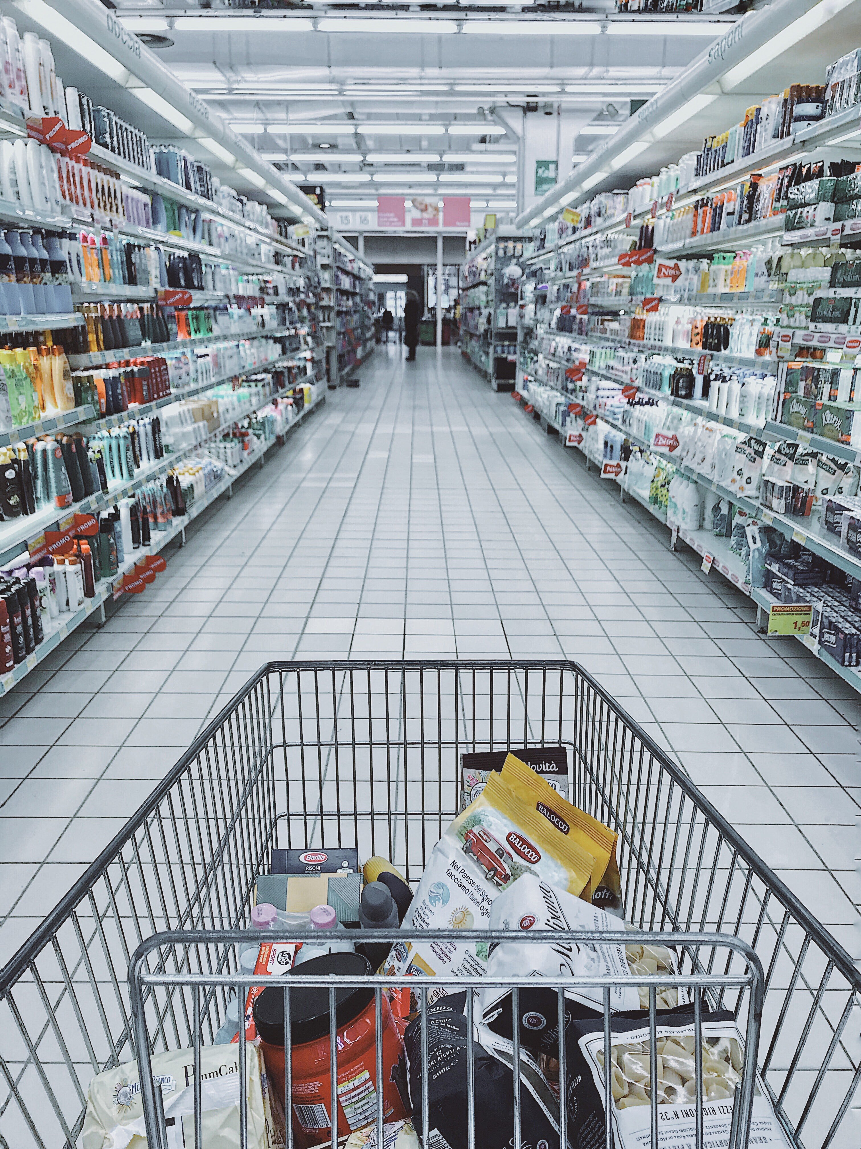 A cart standing in the aisle of a grocery store. | Pexles/ Oleg Magni