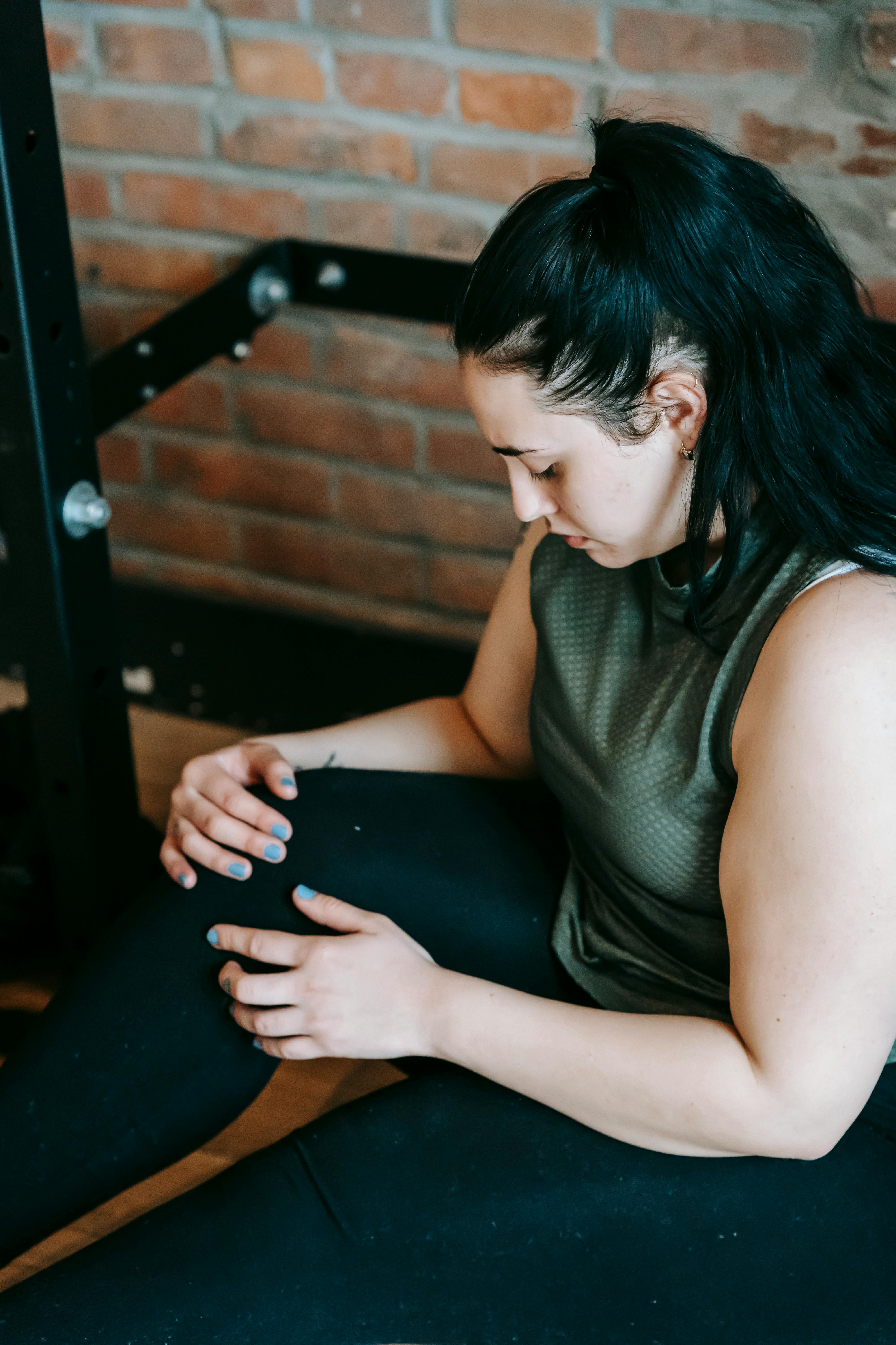 A gym-goer resting and holding her knee after a difficult workout. | Source: Pexels