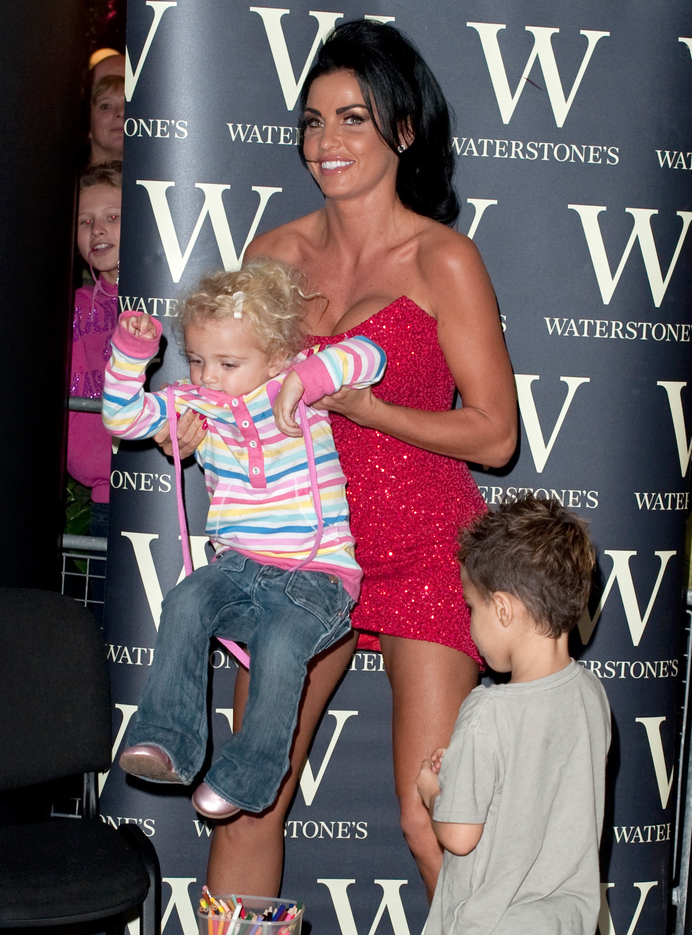 During a book signing event in Essex on October 29, 2009, Katie Price balanced glamour and motherhood in a sparkling red mini dress as she wrangled her lively children. With her daughter in tow and her son by her side, the scene captured the reality star's hands-on approach to parenting, even in the middle of a public appearance.