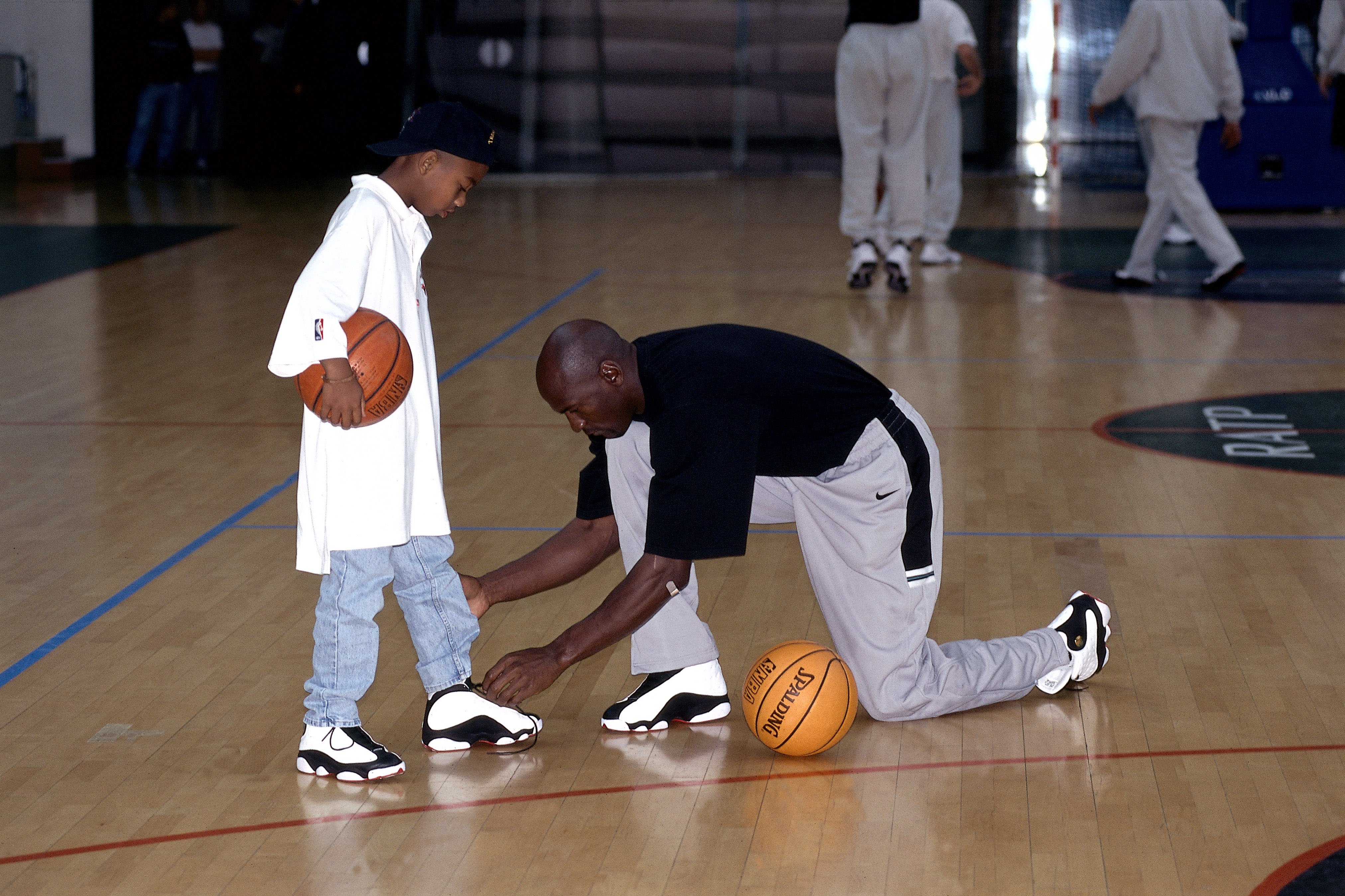 Michael Jordan atando los cordones de los zapatos de su hijo en una práctica de un torneo de baloncesto en París, Francia, en 1998. | Foto: Getty Images